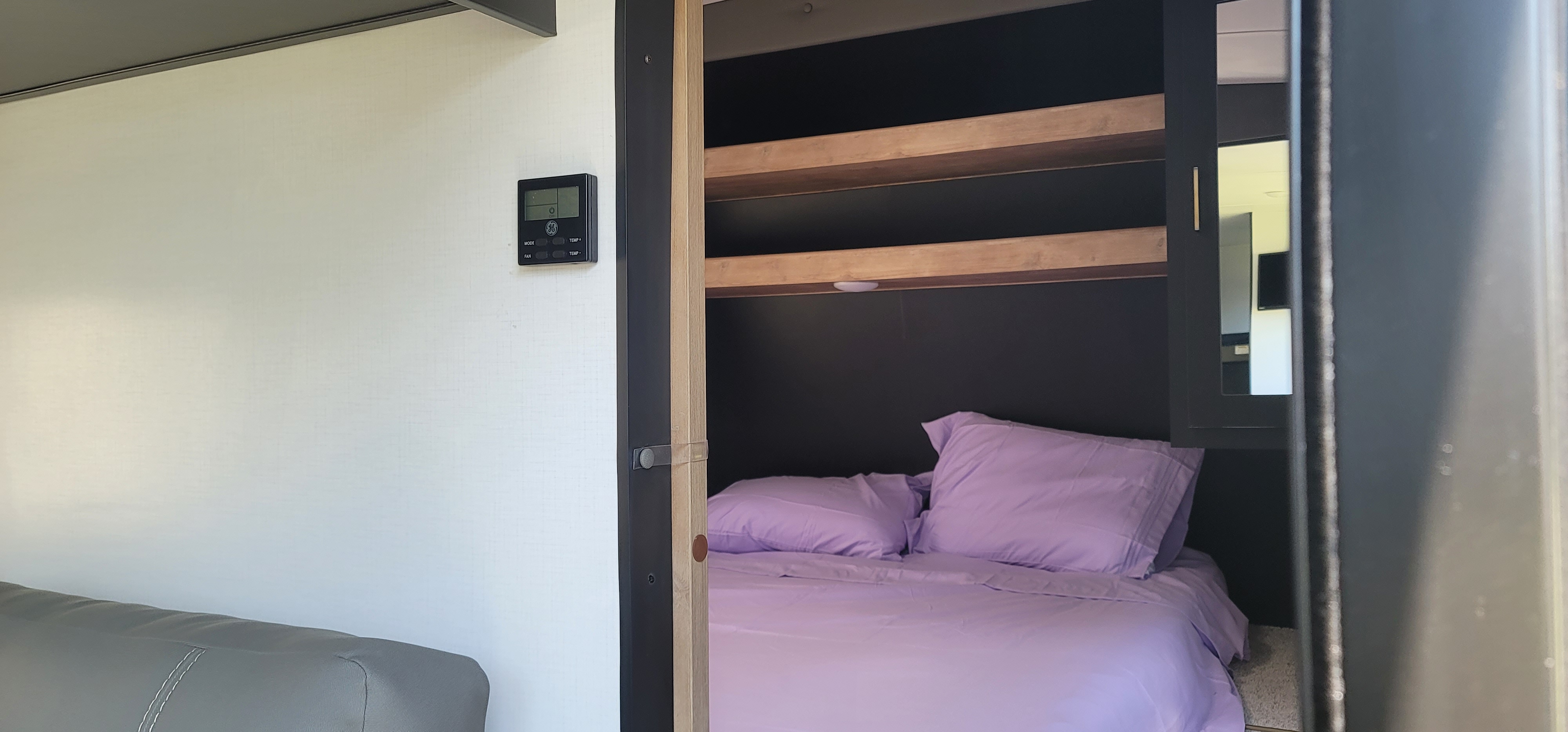 Cozy RV rental bedroom features purple bedding, bunk-style shelving, and a GE climate control unit, ideal for travel.. Keystone RV Springdale 2022