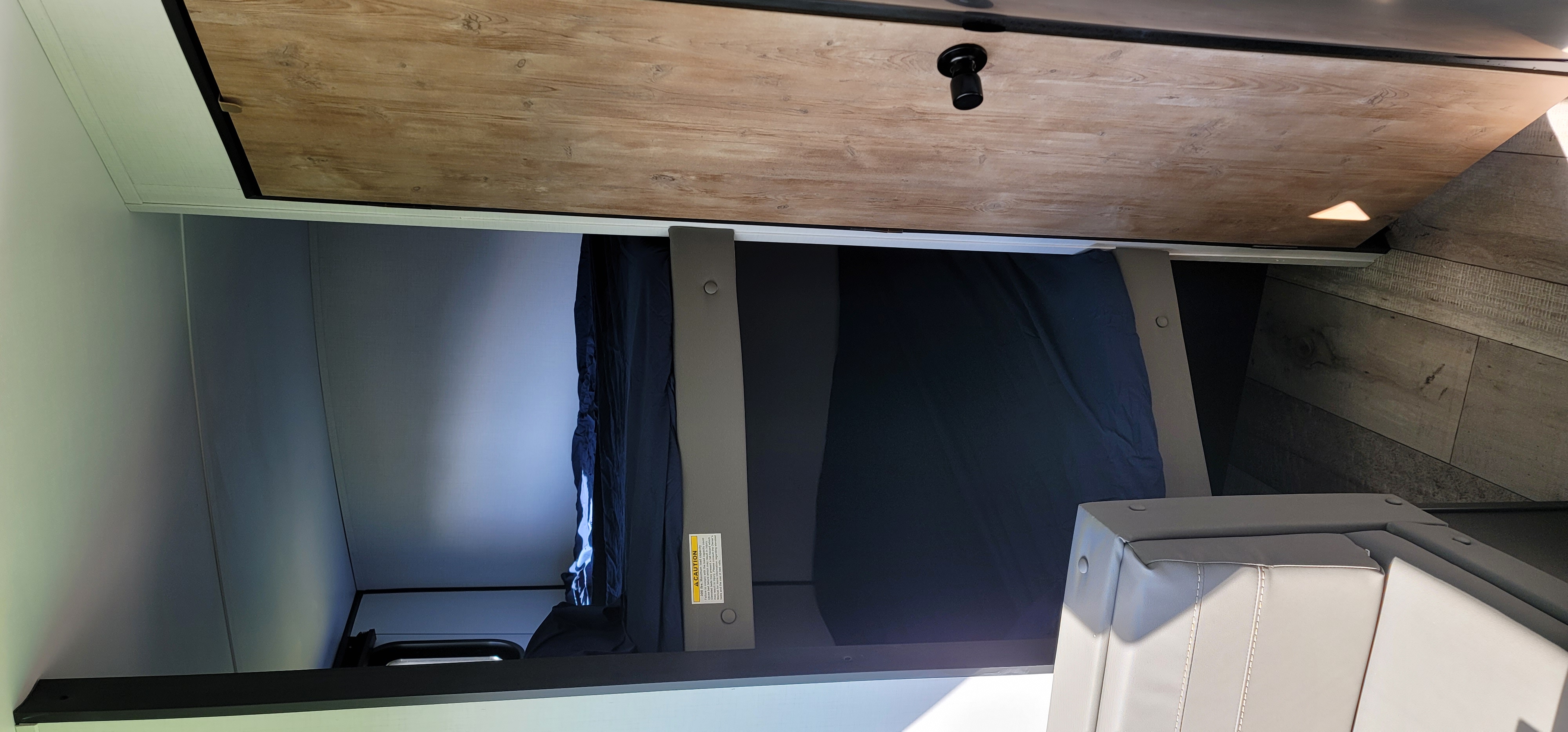 RV rental bunk bed interior: View of an elevated sleeping area with dark bedding, wood ceiling, and upholstered seating.. Keystone RV Springdale 2022