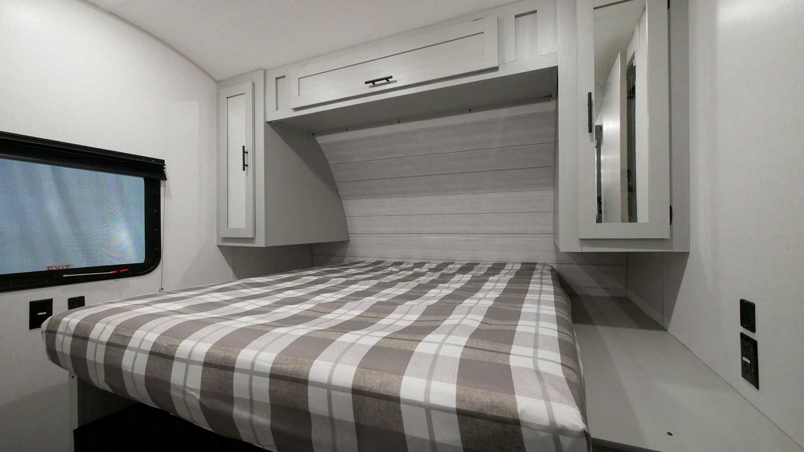 Spacious RV rental bedroom featuring a cozy plaid bed, ample storage via cabinets, and a window for natural light.. Forest River Wildwood 2022
