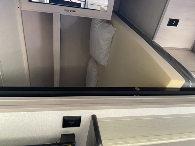 RV rental bed lifts to expose under-bed storage, neatly holding pillows. A foam mattress is visible.. Forest River Tracer 2021