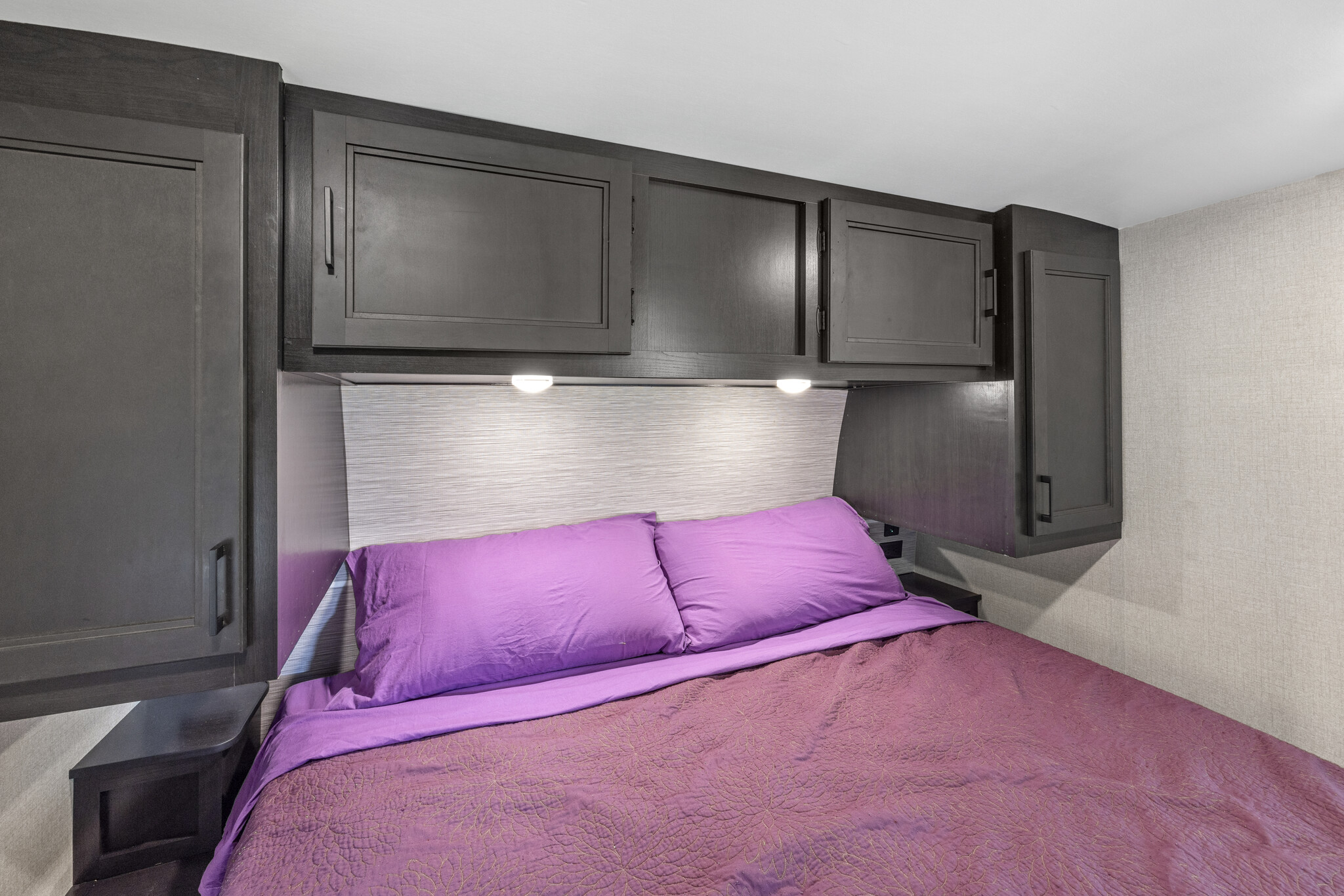 RV rental bedroom with a plush purple bed, overhead dark cabinets, and reading lights, designed for compact comfort.. Highland Ridge RV Open Range Light 2022