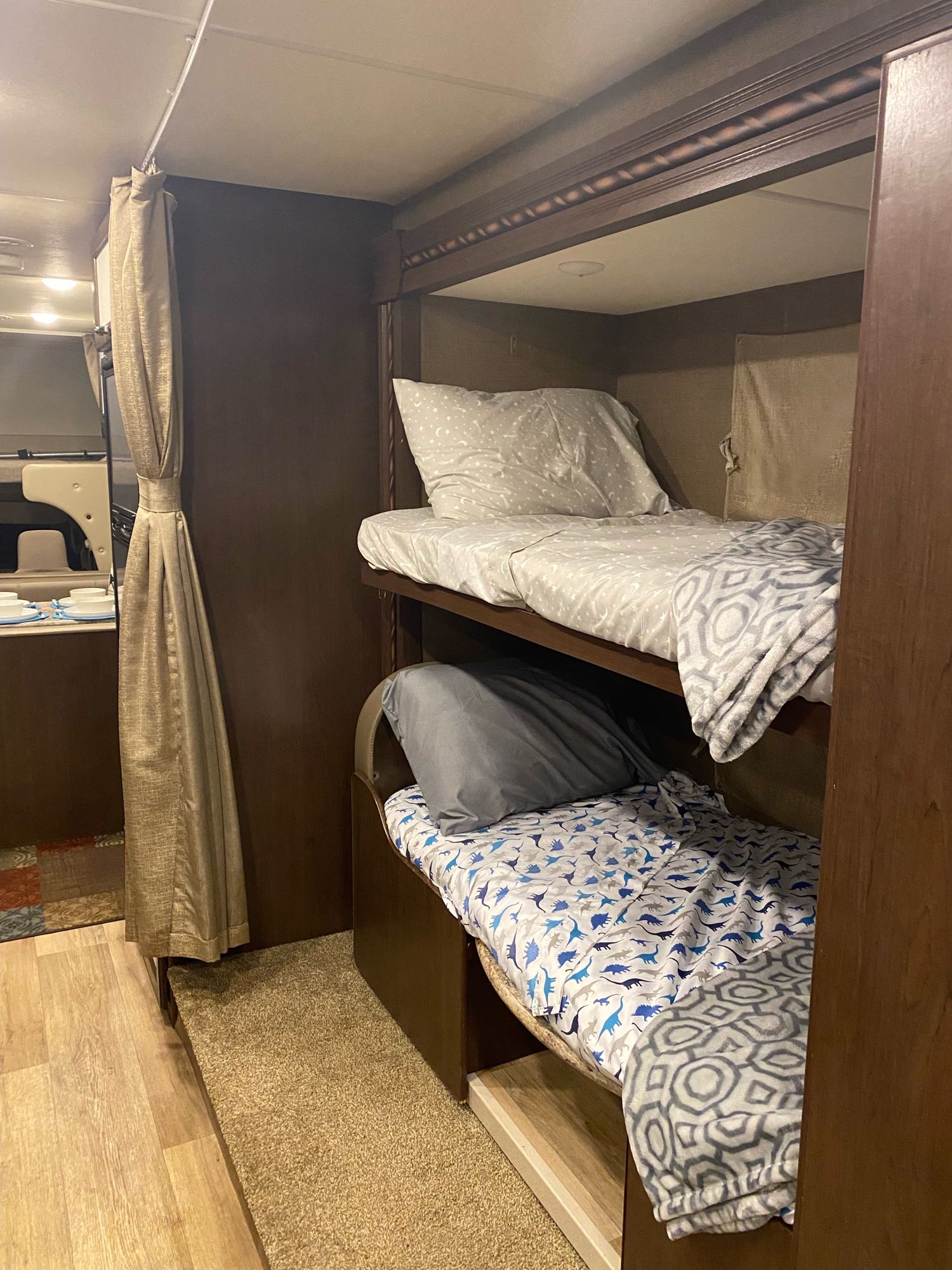 Cozy RV rental interior featuring made-up bunk beds: top with star sheets, bottom with dinosaur bedding. Wood and carpet flooring visible.. Thor Freedom Elite 2017