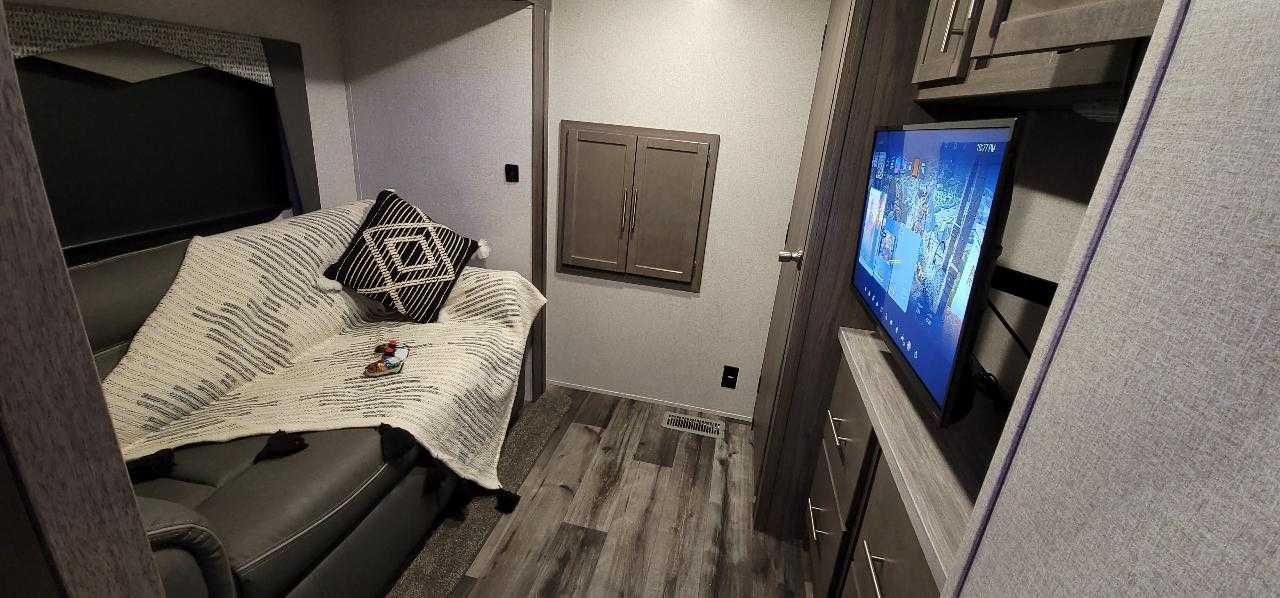 Inside a cozy RV rental: living area with a comfy sofa, patterned blanket, and wall-mounted TV.. Crossroads RV Volante HP 2022