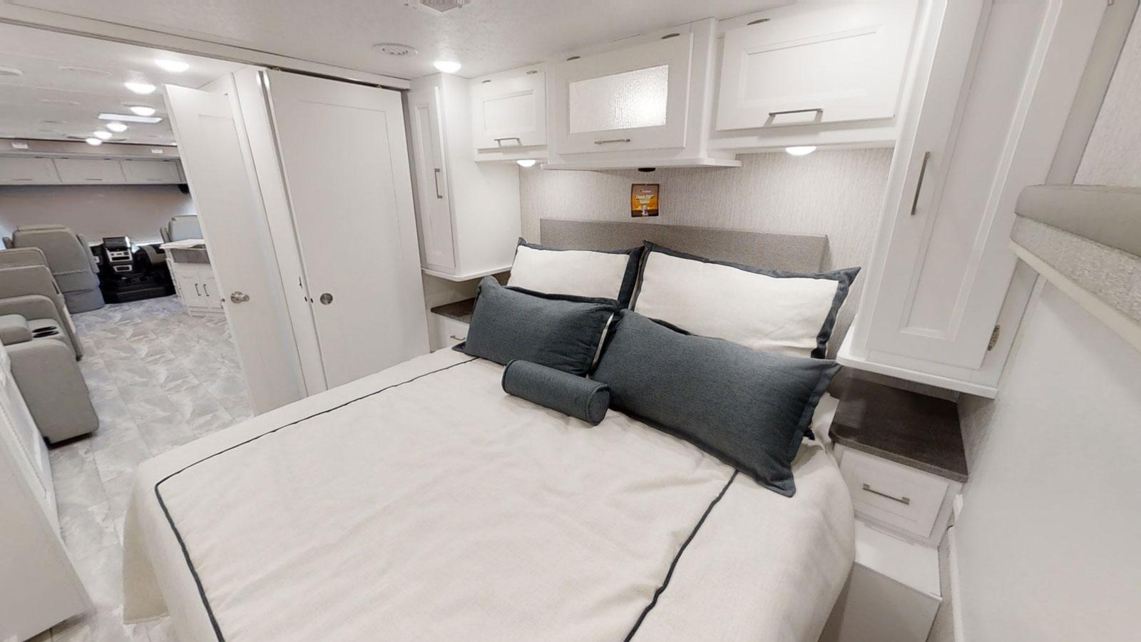 Cozy RV rental bedroom with clean white cabinets, a comfortable bed with grey pillows, and access to the front living space.. Coachmen Encore 2021