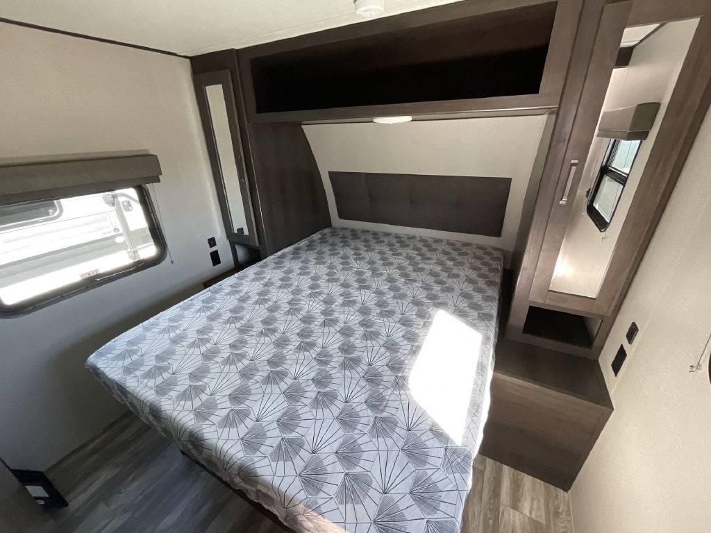 Comfortable RV rental bedroom with a bed, built-in storage, and window. Mirrored cabinets are on the right.. Grand Design Transcend Xplor 2022