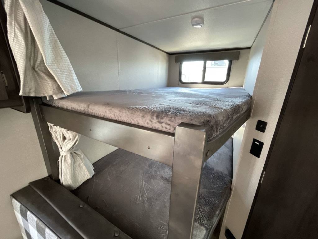 RV rental interior: cozy bunk beds (upper and lower) with soft gray blankets, providing compact sleeping space for trips.. Grand Design Transcend Xplor 2022