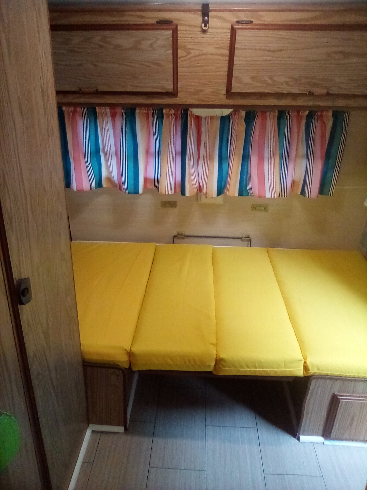 Cozy RV rental interior with bright yellow cushions for seating/bed, striped curtains, and wood cabinets. Ready for adventure!. Sunline Saturn 1987