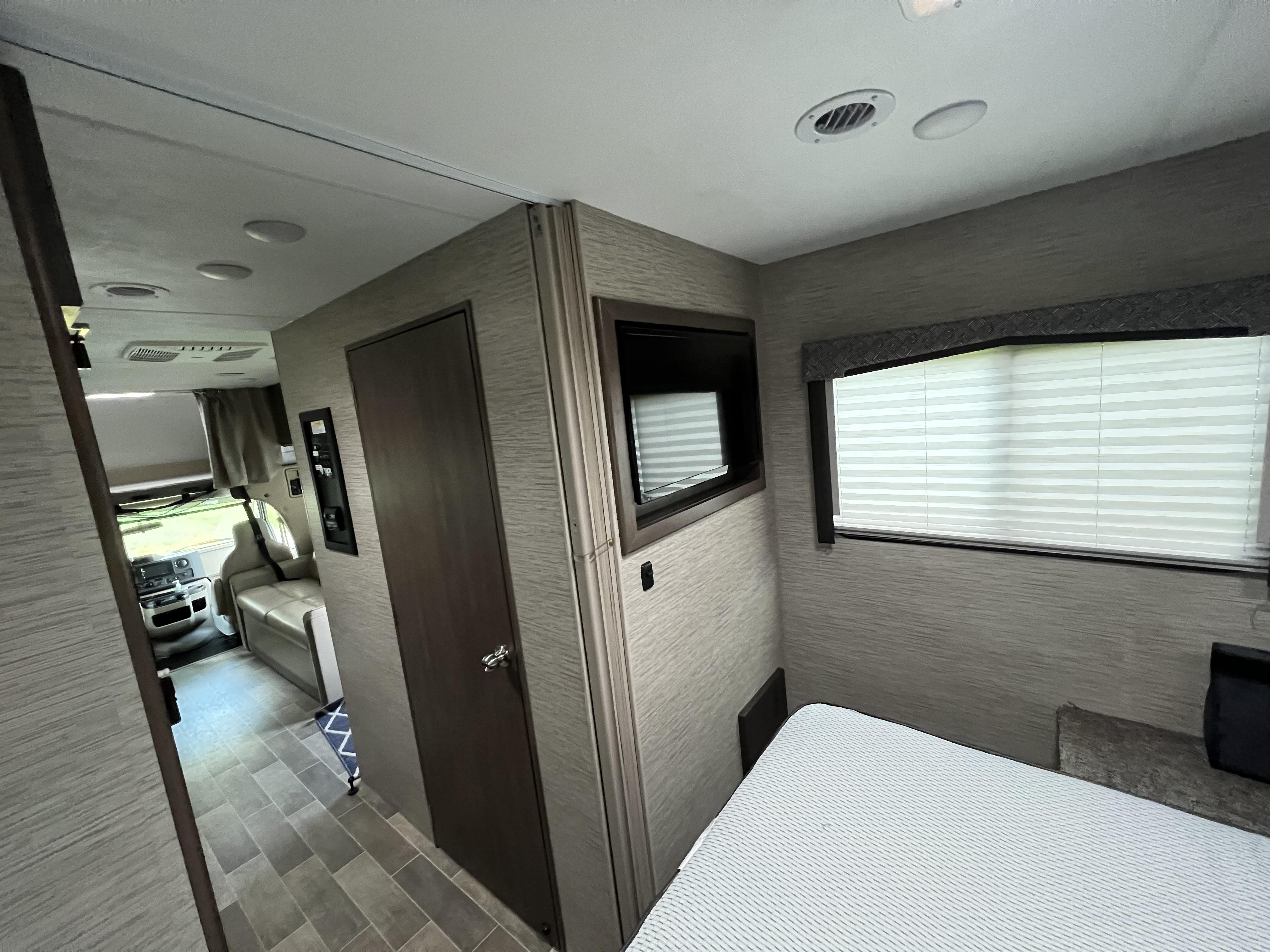 Comfortable rv rental interior, featuring a cozy bedroom with window & TV, plus a living area view. Ideal for road trips.. Thor Chateau 2022