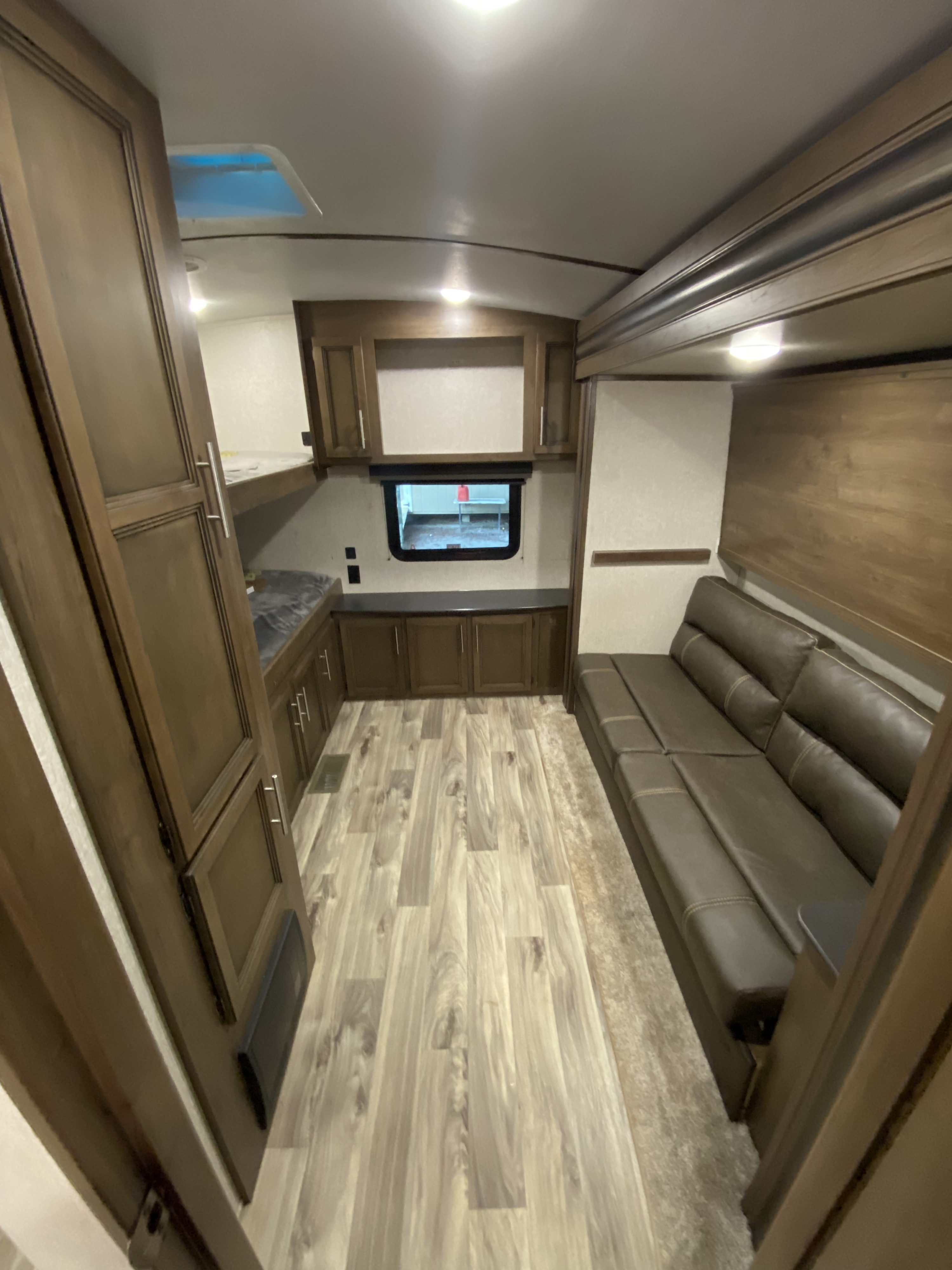 Modern RV rental interior with a long brown sofa, bunk beds, wood-look floor, and built-in cabinets.. Keystone Cougar Half-Ton 2021