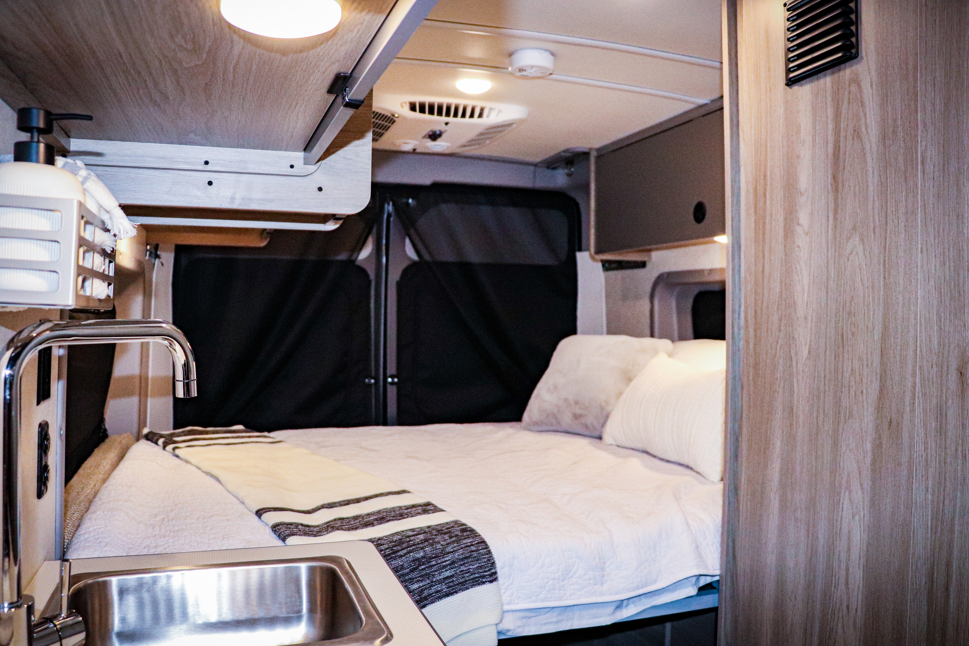 Experience comfort in this RV rental: a cozy bed, sleek kitchen sink, and bright lighting in a wood-paneled interior.. Winnebago Solis 2022