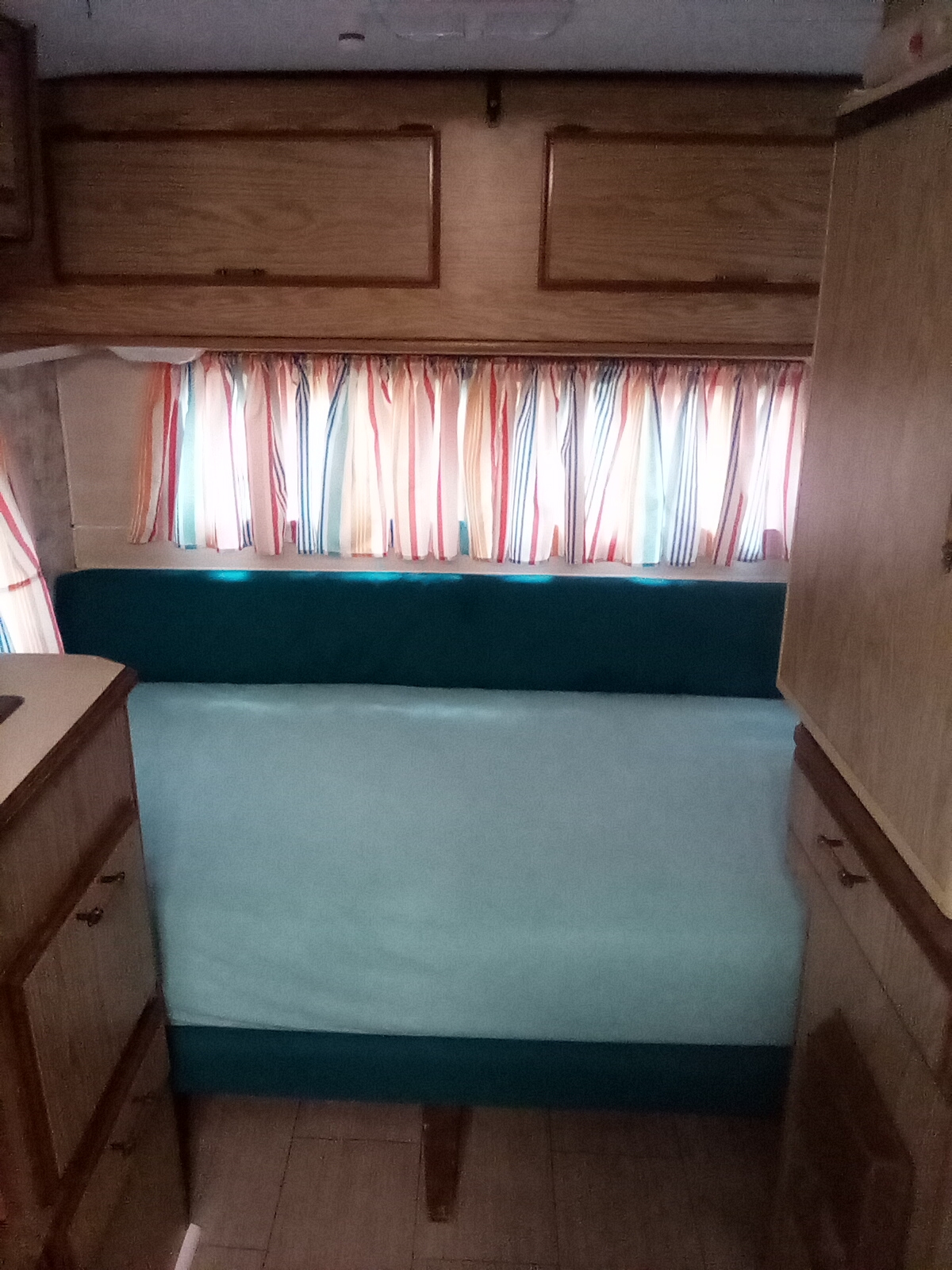 RV rental interior: teal bench seating, vibrant striped curtains, and practical wood cabinetry.. Sunline Saturn 1987