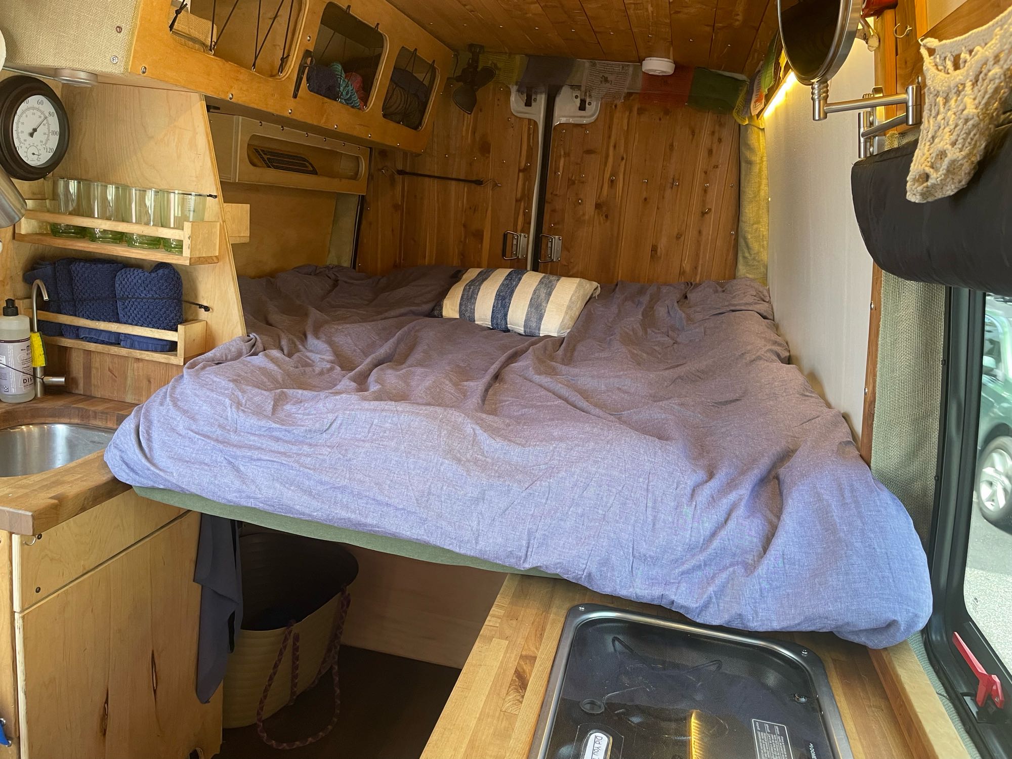 Cozy RV rental interior with a comfortable bed, compact kitchen, and wood paneling. Ideal for travel adventures.. Mercedes-Benz Sprinter 2016