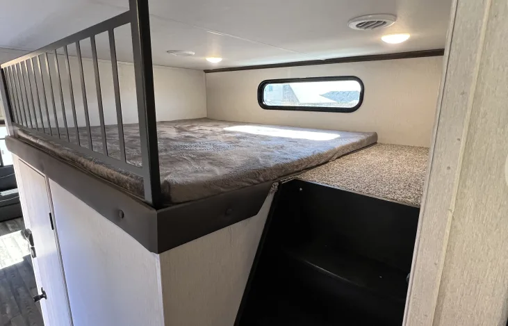Inside an RV rental: a large upper bunk bed with a safety railing, a window, and stairs leading up.. Forest River Cardinal 2022