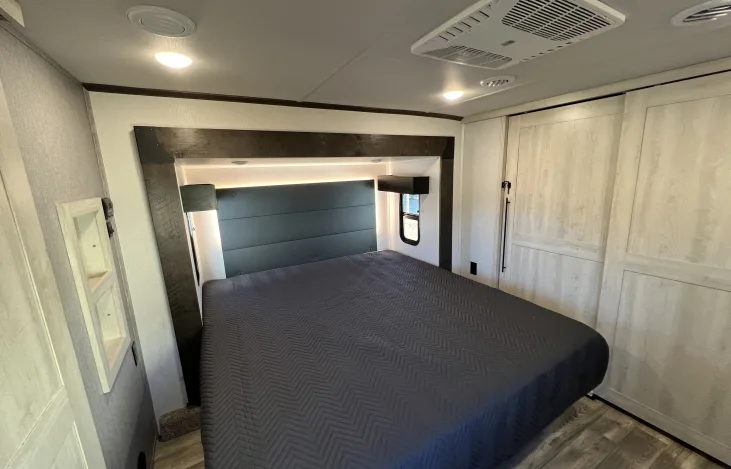 Step into this comfortable RV rental bedroom, featuring a large bed, ambient lighting, and convenient sliding doors.. Forest River Cardinal 2022