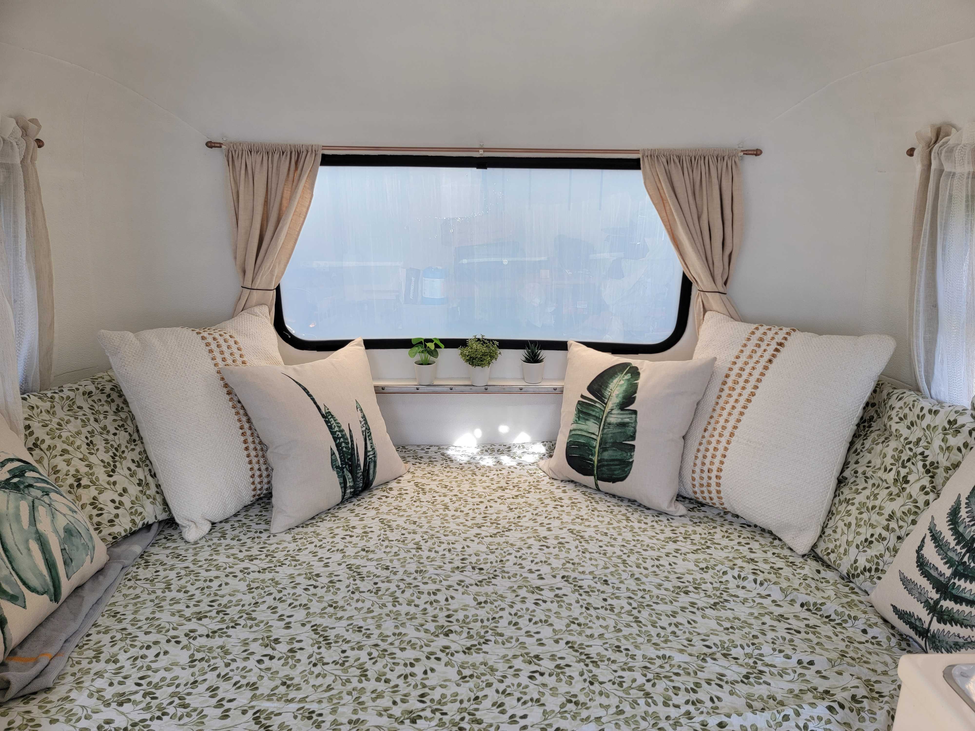 RV rental cozy interior with leaf-patterned bedding, pillows, and small plants by the window.. Boler Original 1971
