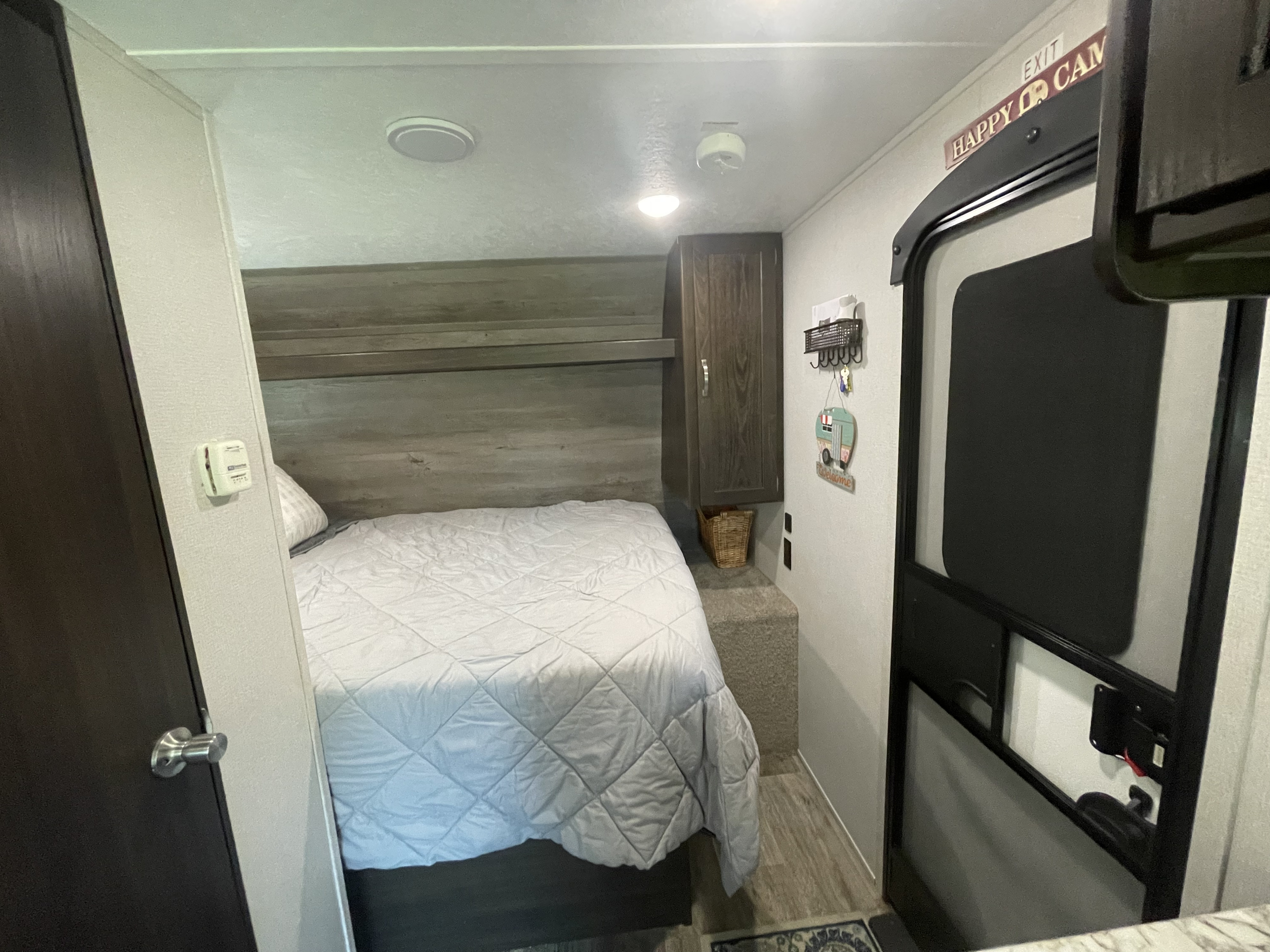Cozy RV rental bedroom with a quilted bed, built-in storage, and the entry door, designed for comfortable travel.. Springdale 1750RD 2020