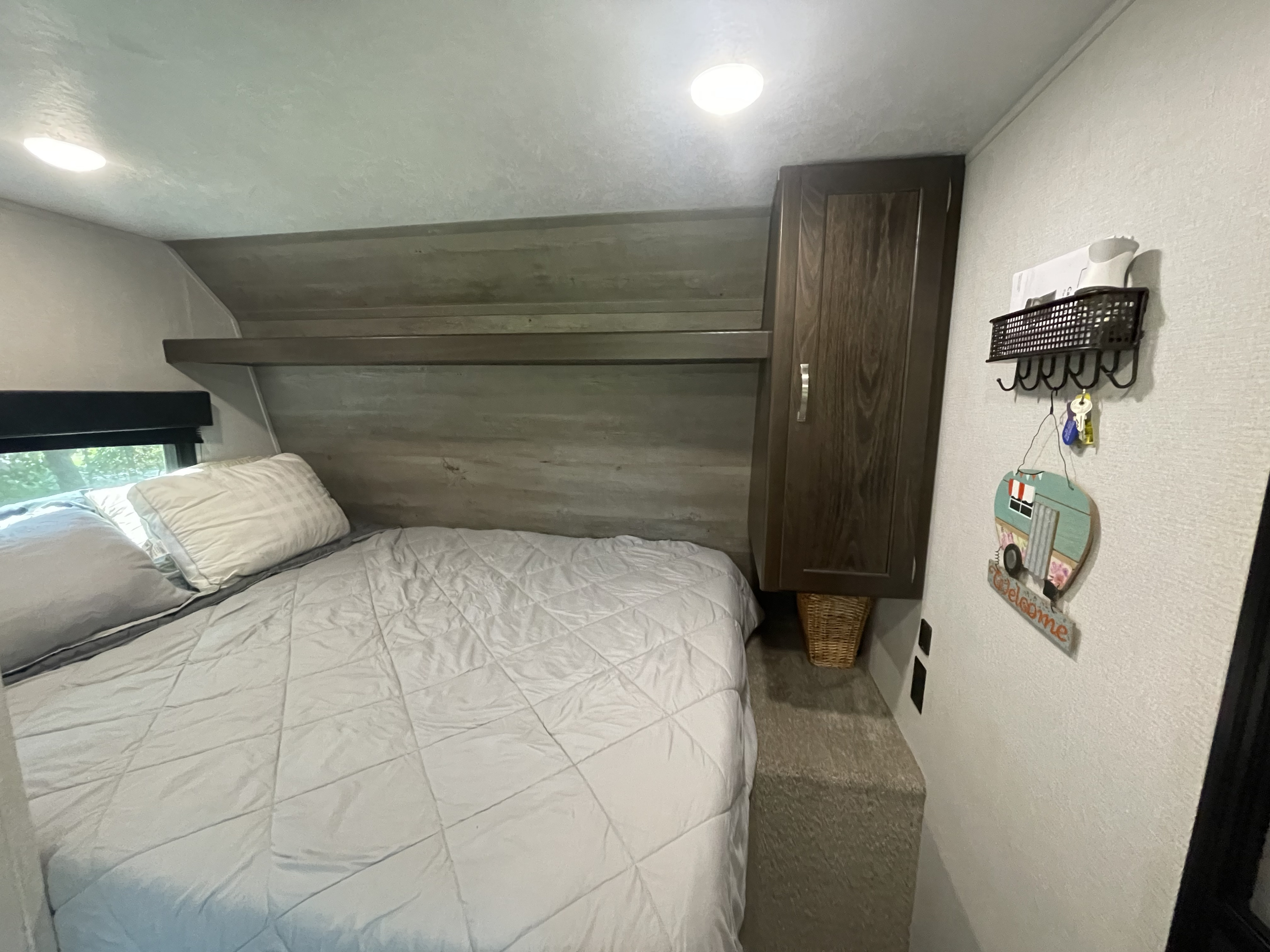 Cozy RV rental bedroom with a comfortable bed, light bedding, overhead storage, cabinet, and welcoming camper decor on the wall.. Springdale 1750RD 2020