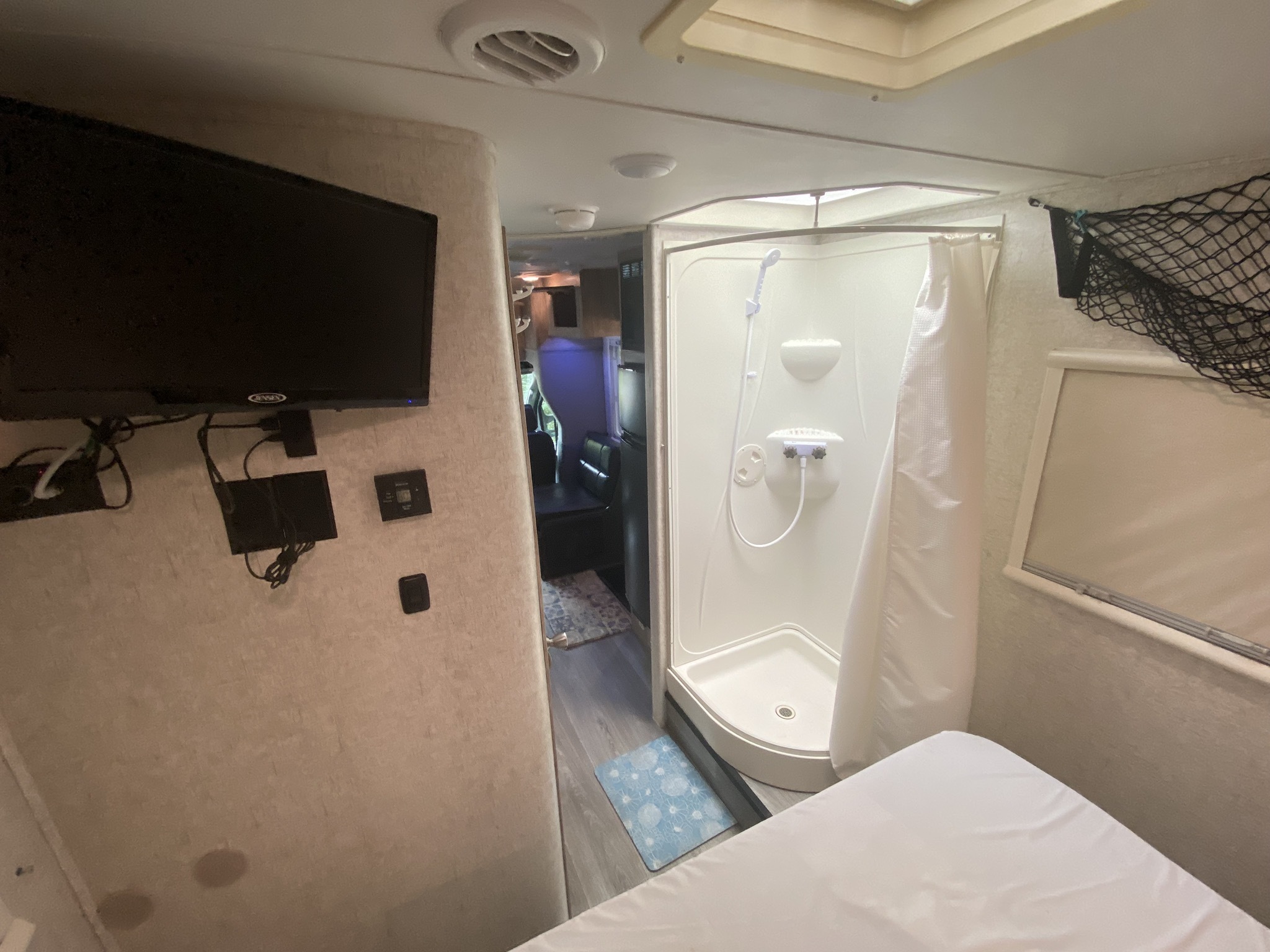RV rental interior showing bedroom area with TV, compact shower on right, and hallway to the front living space.. Forest River Sunseeker 2017