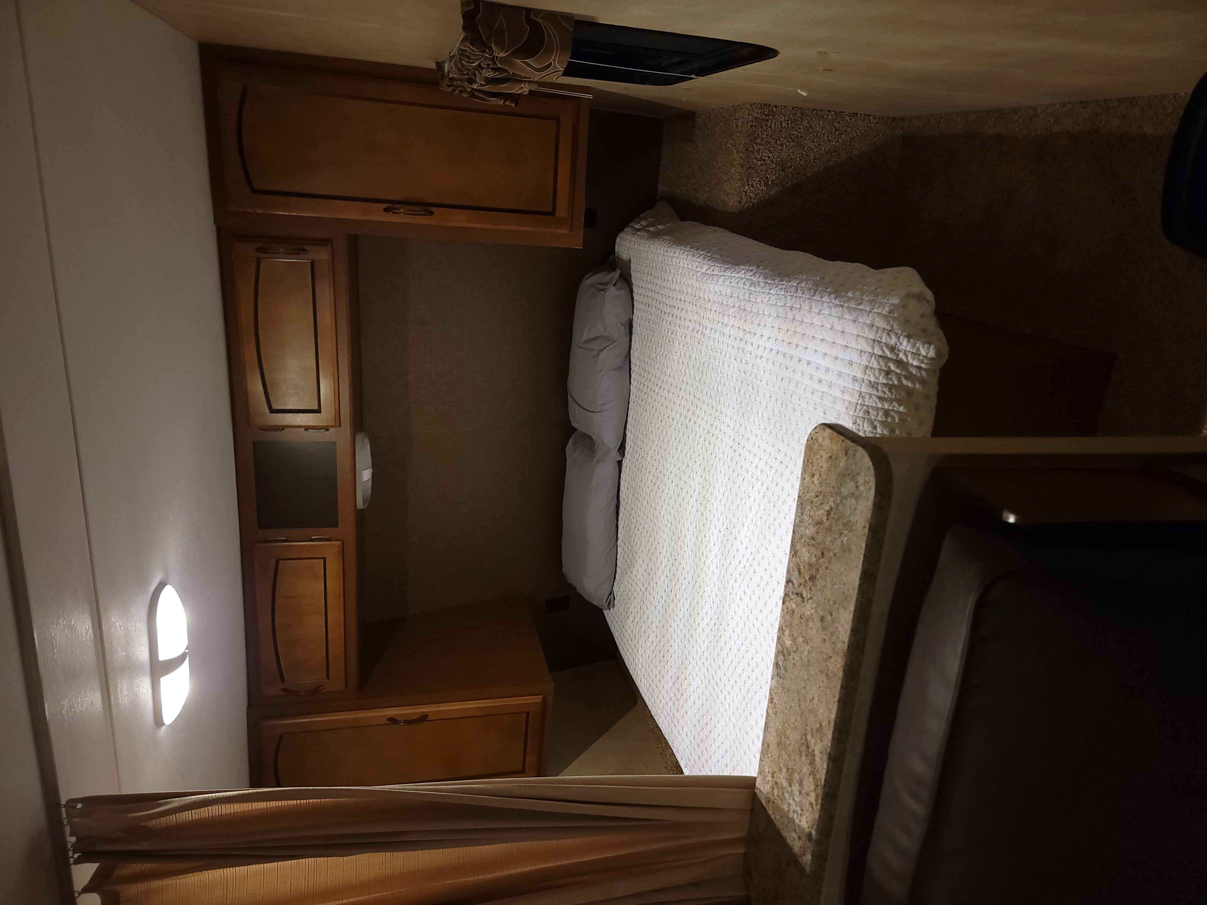 Cozy RV rental bedroom with a comfortable bed, overhead wood cabinets, and a glowing bedside light next to a compact counter.. Keystone Summerland 2015