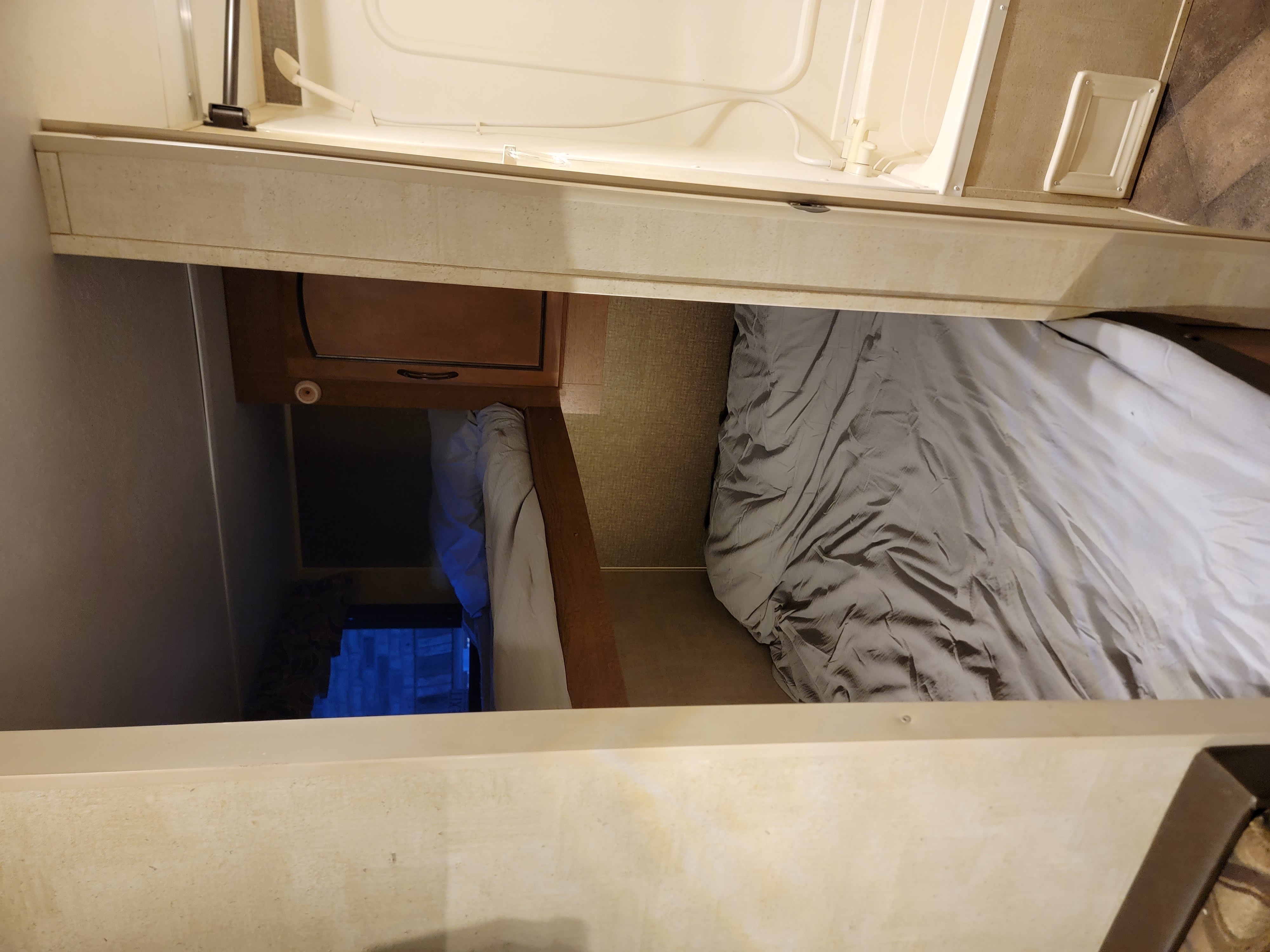 Inside an **RV rental**, a compact bedroom with gray bedding, wooden cabinets, and a small built-in shower stall.. Keystone Summerland 2015
