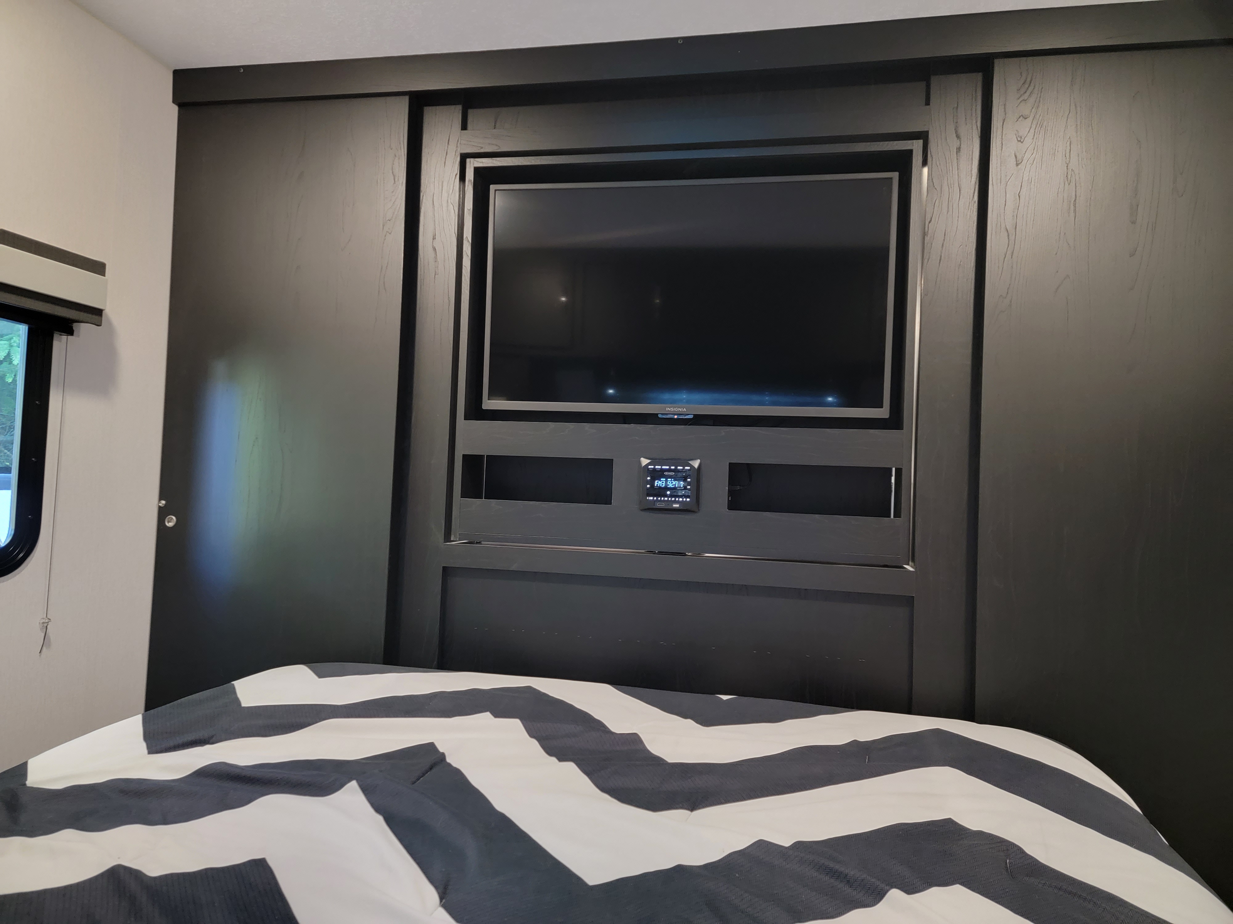 RV rental bedroom featuring a built-in TV and media system above a comfortable black and white striped bed.. Coachman Freedom Express 2022