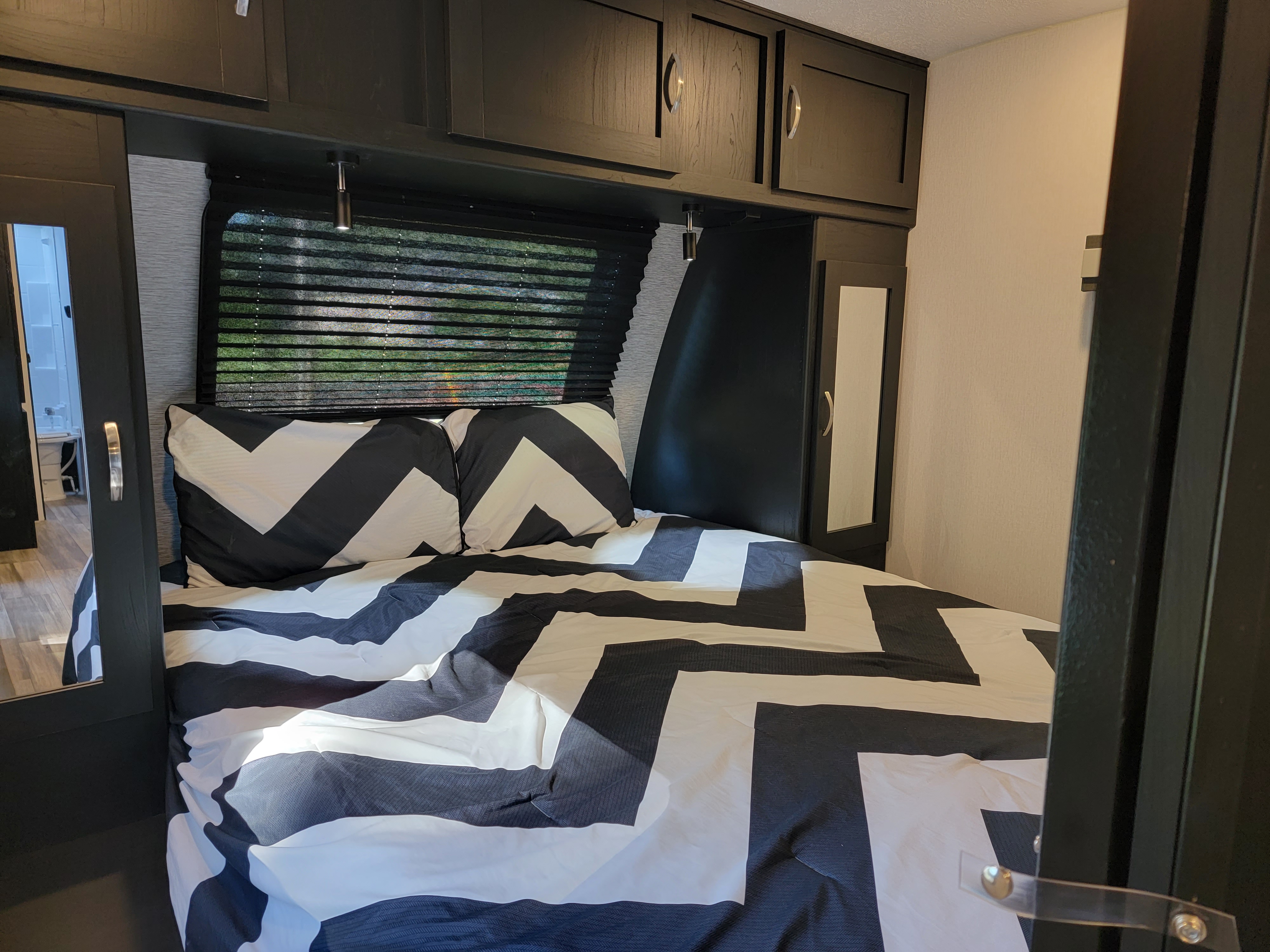 Explore a modern RV rental bedroom: black and white bed, built-in mirrored closets, and practical overhead cabinets.. Coachman Freedom Express 2022