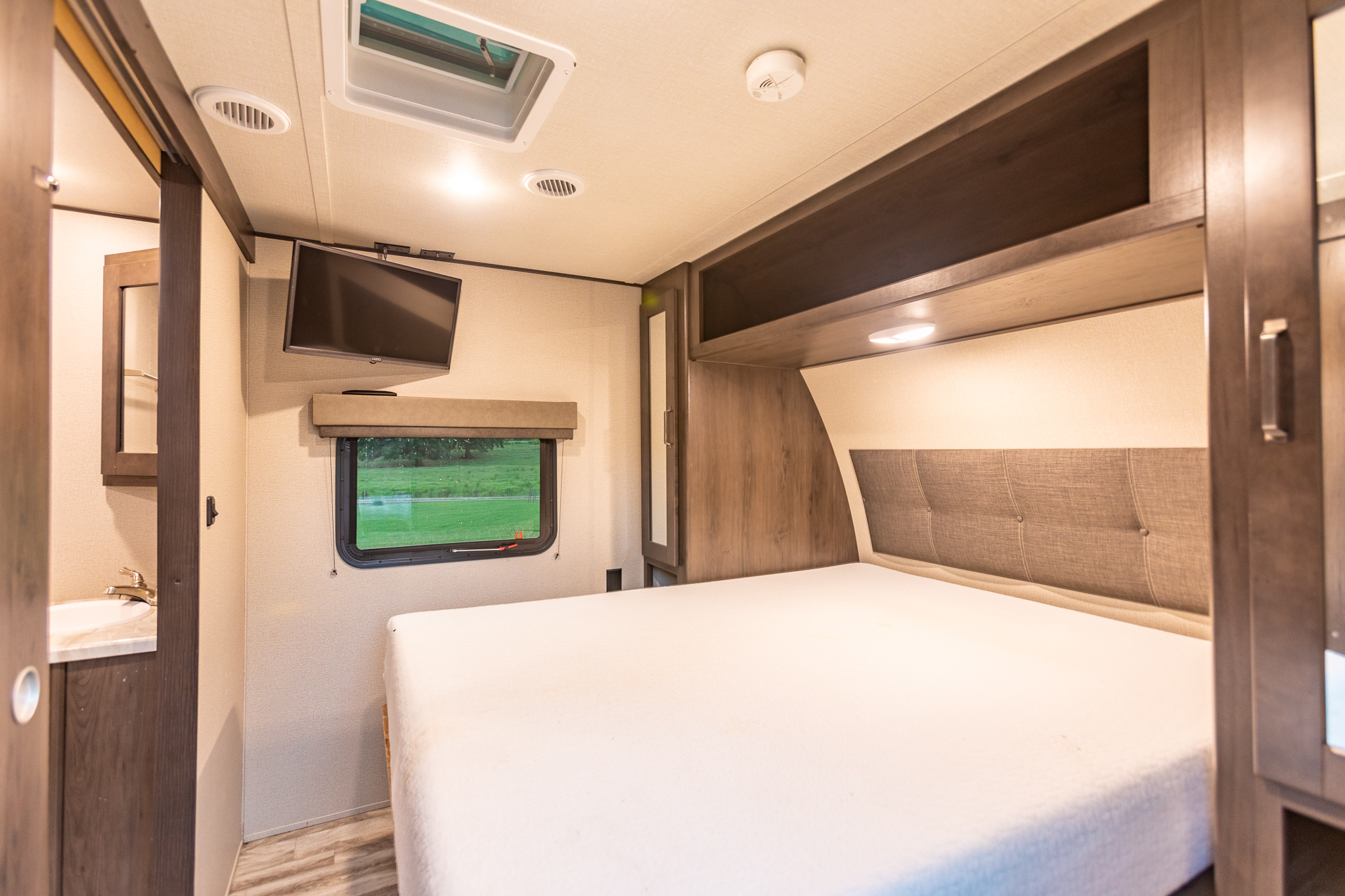 Explore this compact **rv rental** bedroom featuring a comfy bed, wall-mounted TV, storage, and a window view.. Grand Design Transcend Xplor 2021