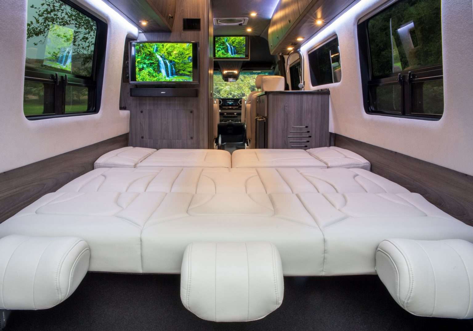 Luxurious RV rental interior with large white beds, dual TVs, and a compact kitchenette. Perfect for comfortable travel.. Grech Motors Strada 2022