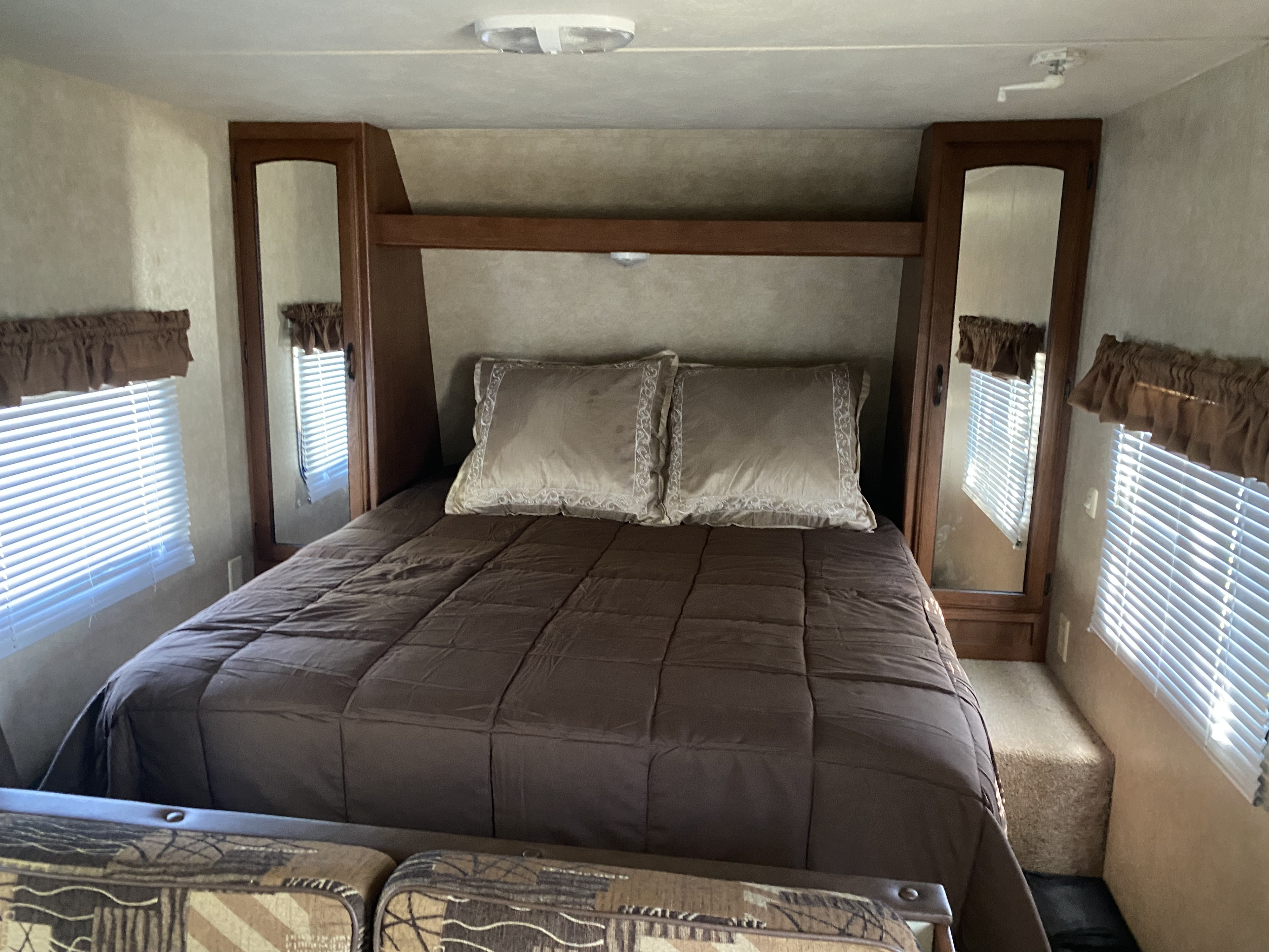 This cozy RV rental bedroom features a comfortable bed with decorative pillows, built-in mirrored storage, and windows with blinds.. Forest River Salem Cruise Lite 2015