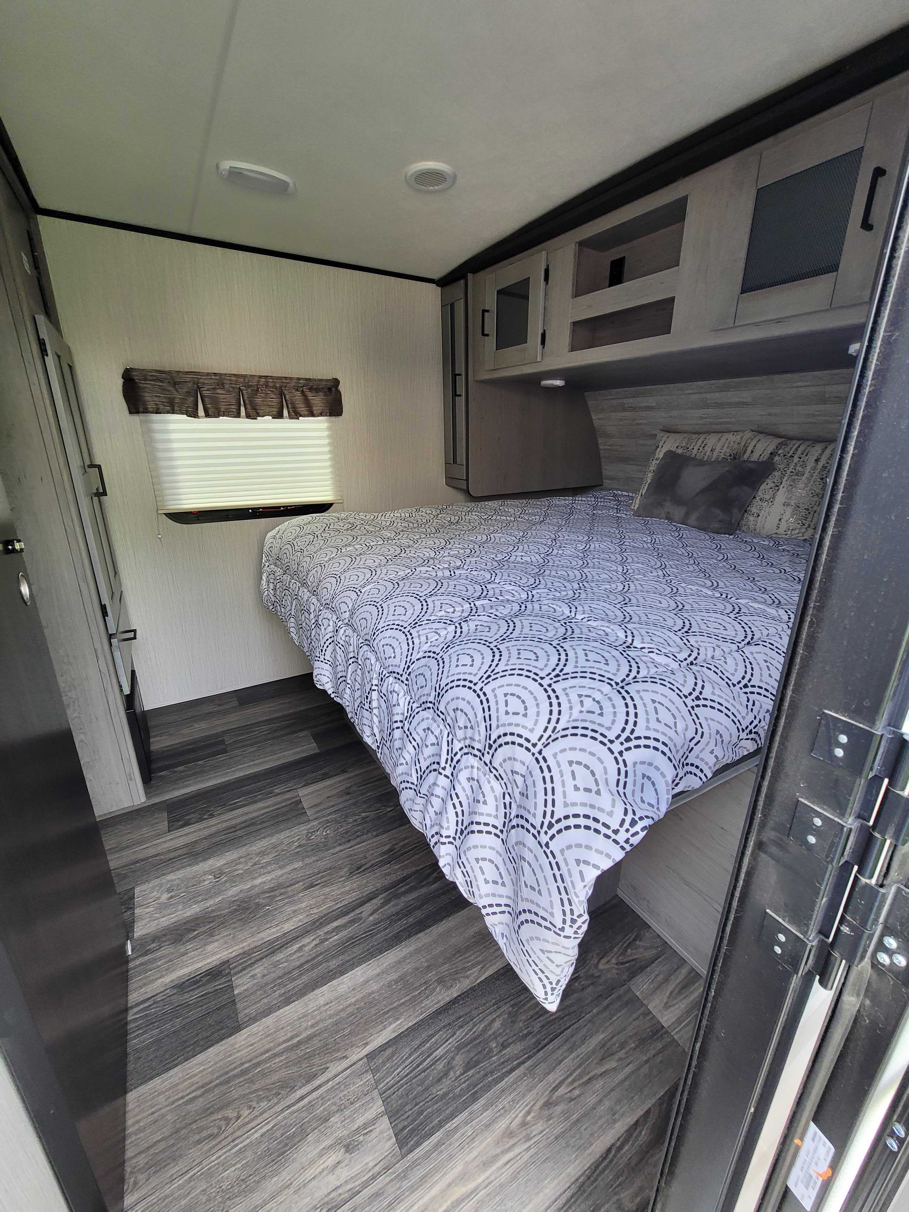 Relax in this RV rental's cozy bedroom, featuring a patterned comforter, sleek overhead cabinets, and wood-look flooring.. Heartland RVs Mallard 2021