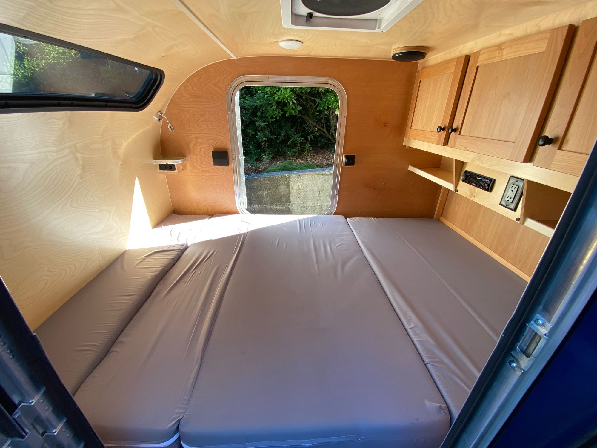 Spacious sleeping area with a comfy bed inside this compact RV rental. Features warm wooden interior, storage, and windows.. Aero Teardrop High Clearance (HC) Steelie 2022