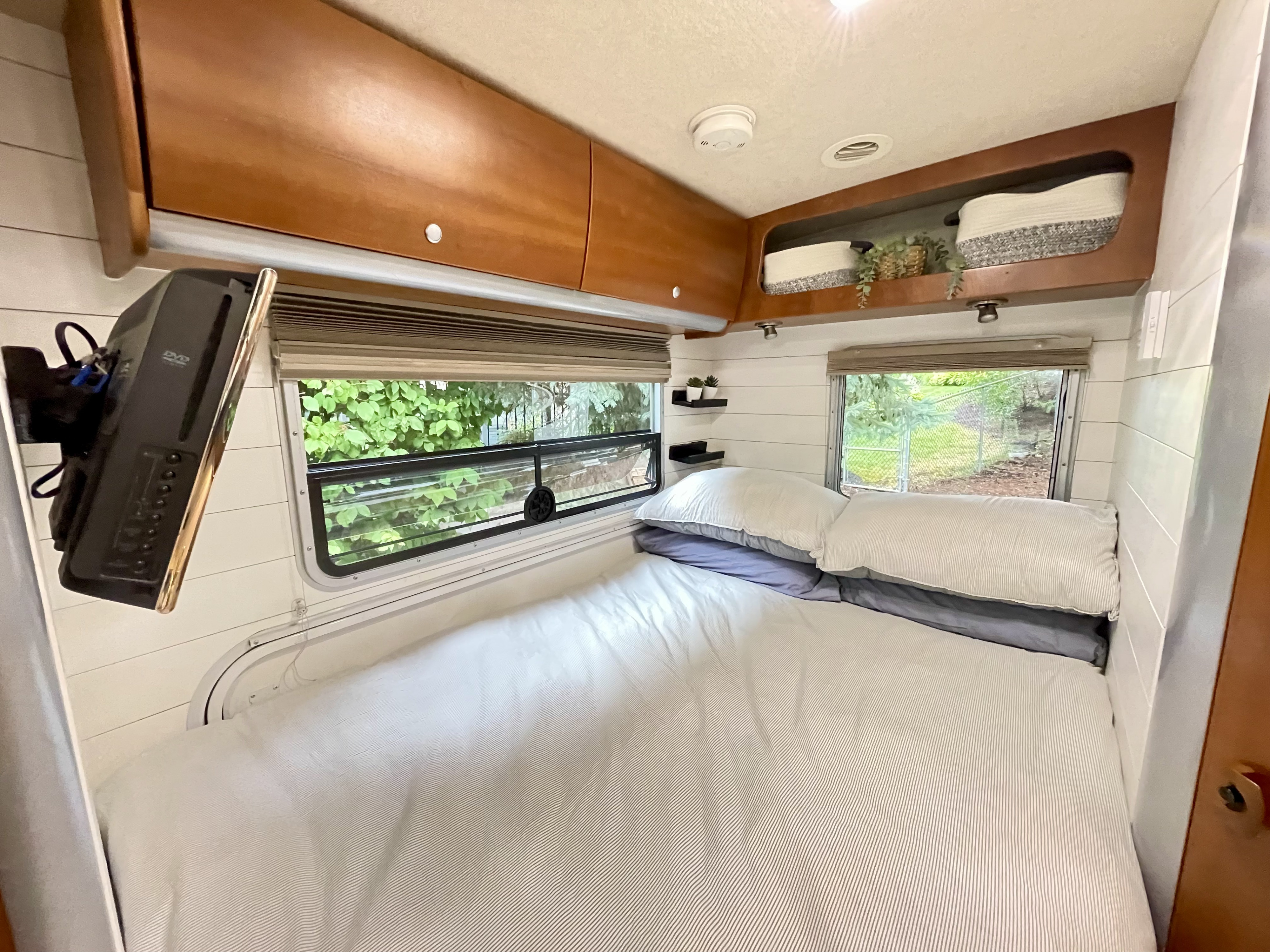 Cozy RV rental bedroom with striped bedding, overhead storage, windows, and a wall-mounted TV for comfortable travel.. Winnebago View 2006