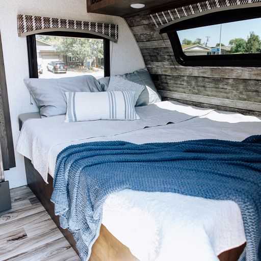 Relaxing RV rental bedroom. Features a comfy bed with blue throws, wood-paneled walls, and exterior views.. Venture Sonic 2022