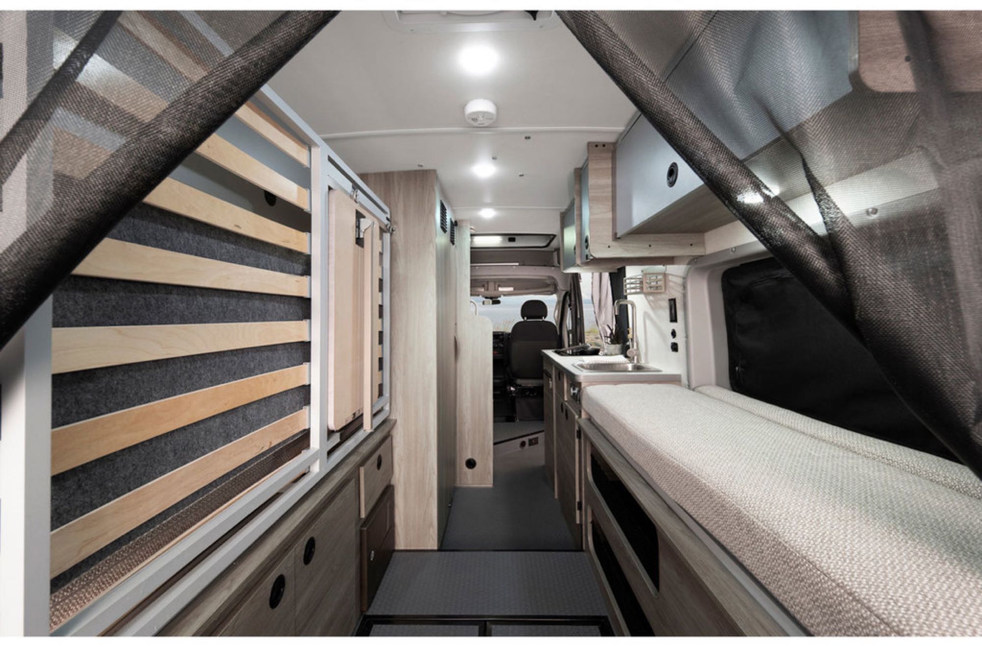 RV rental interior: A compact living space featuring a bed frame (left), galley kitchen with sink, and cushioned bench (right).. Winnebago Solis 2023
