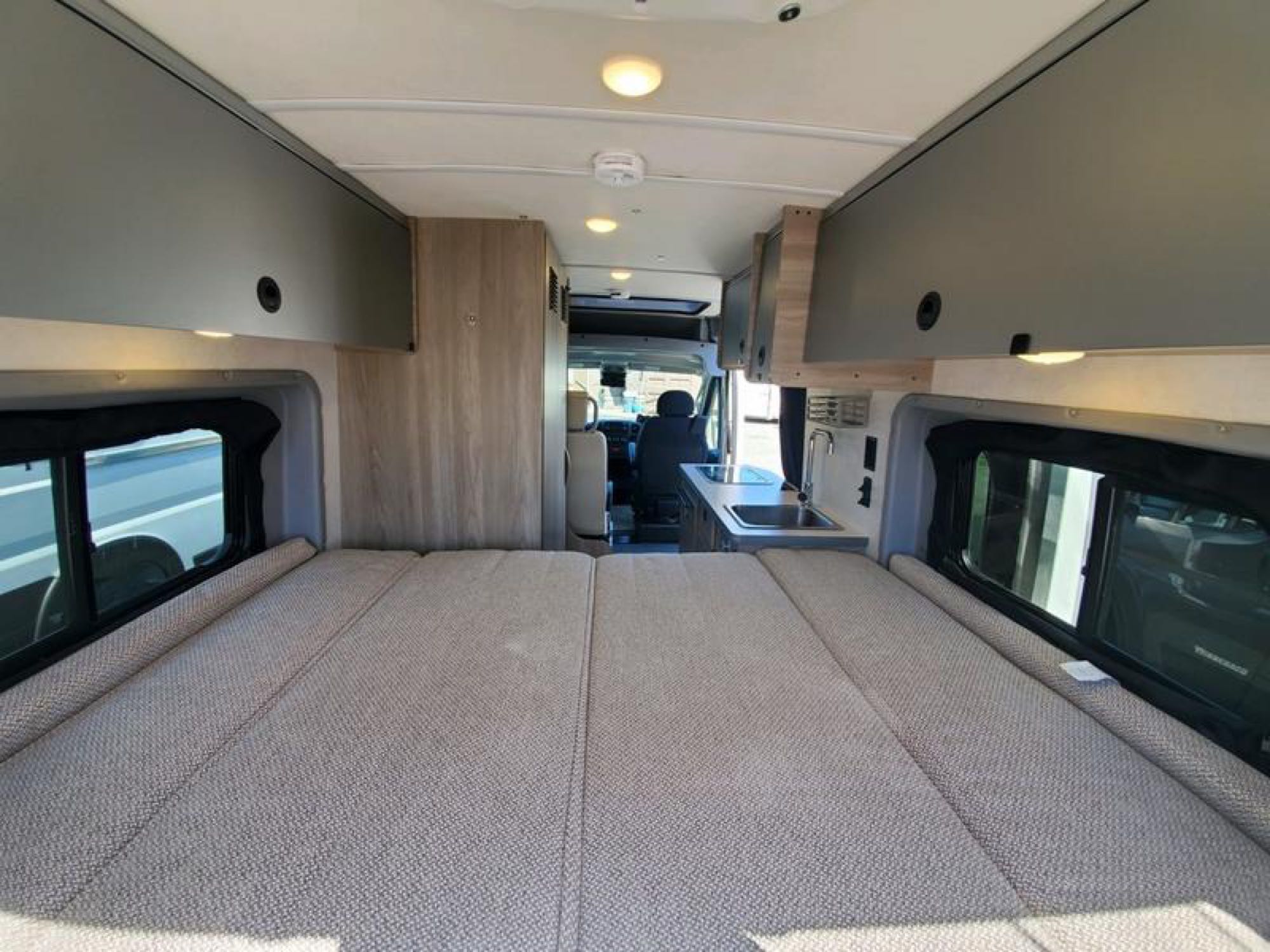 Spacious RV rental interior featuring a comfortable bed, overhead storage, and compact kitchen area.. Winnebago Solis 2023