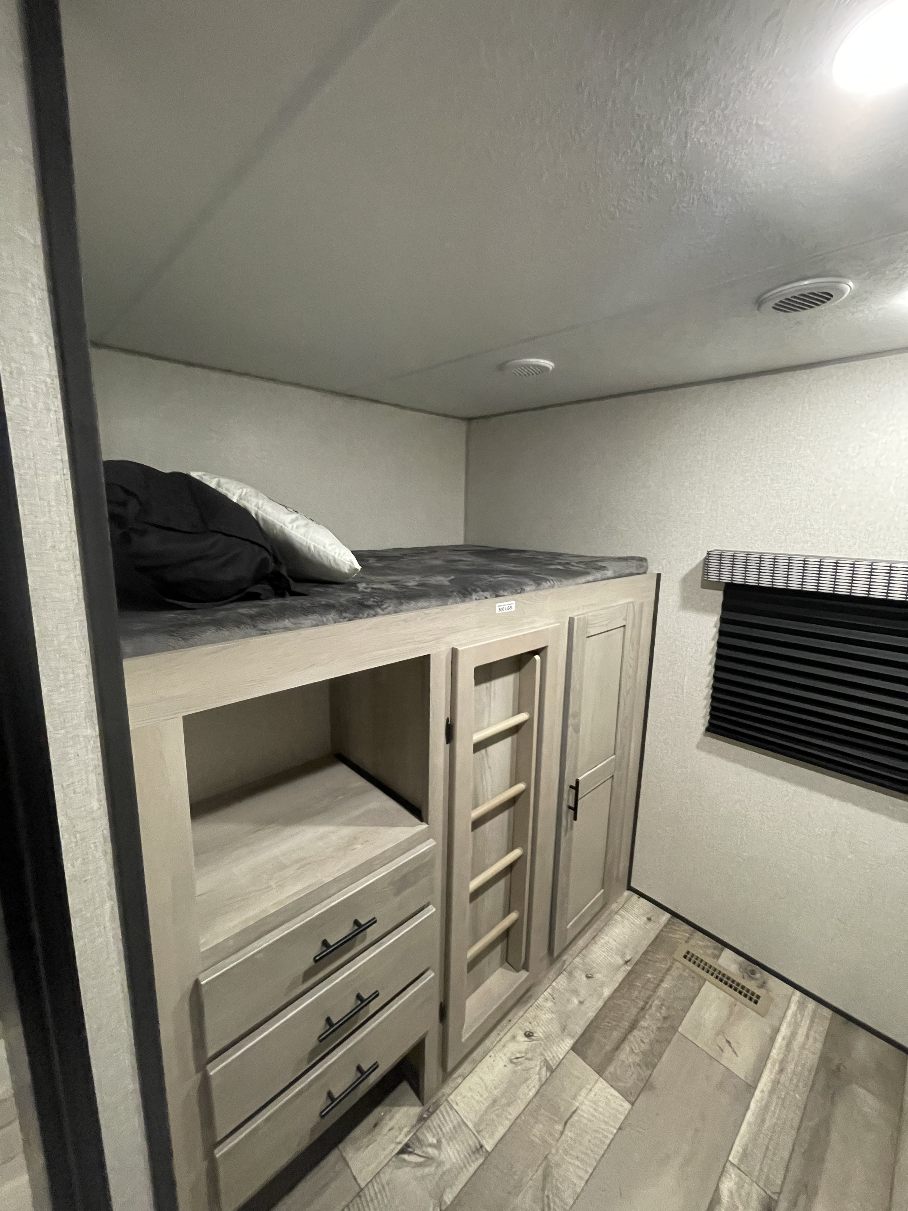 RV rental bunk room: a comfortable bed with pillows, plus integrated storage (drawers, cabinet, ladder). Window with blind.. KZ Connect 322BHK 2022