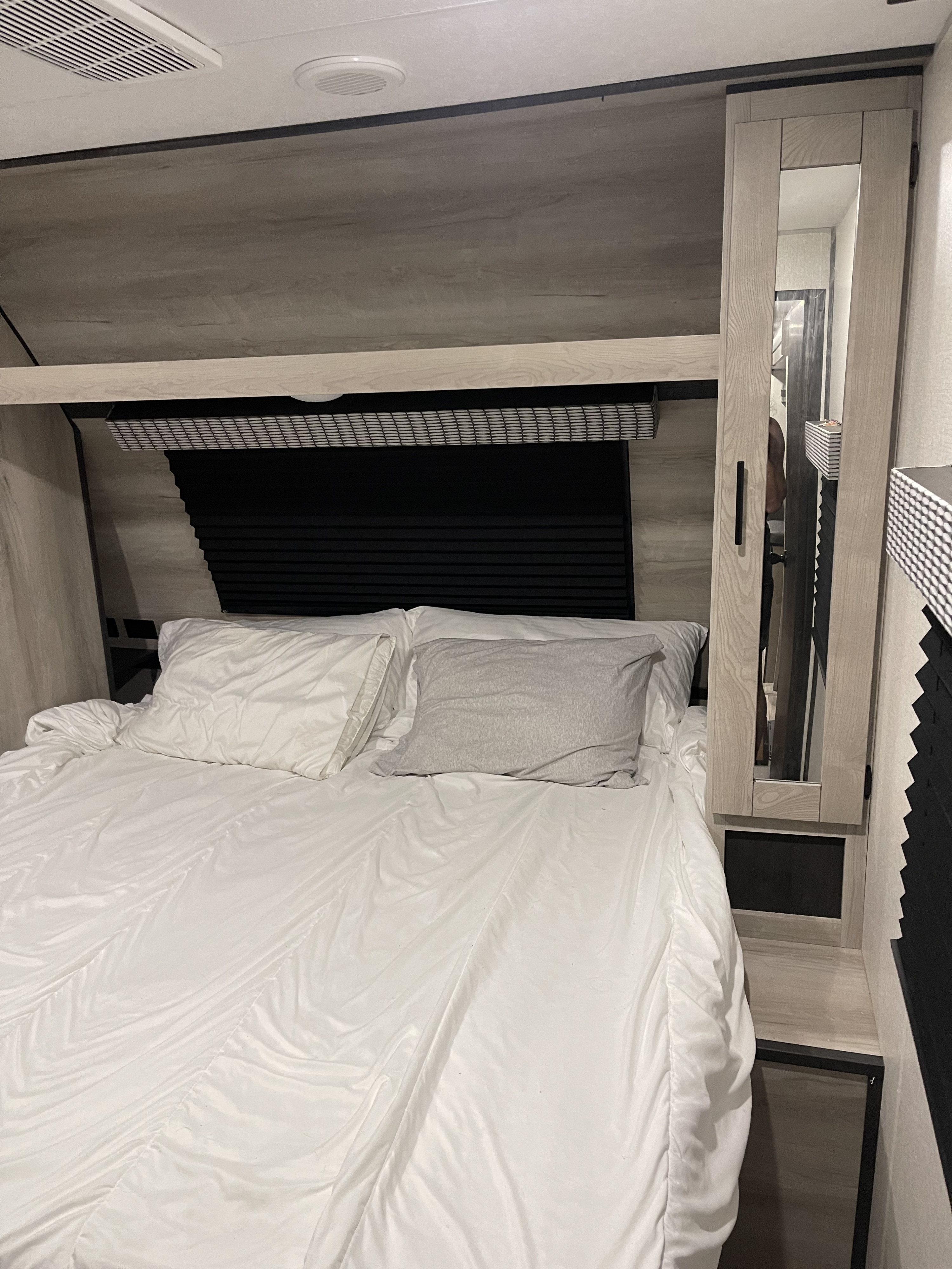 Relax in this RV rental bedroom: a comfy bed, functional overhead storage, a mirrored cabinet, and window blinds.. KZ Connect 322BHK 2022