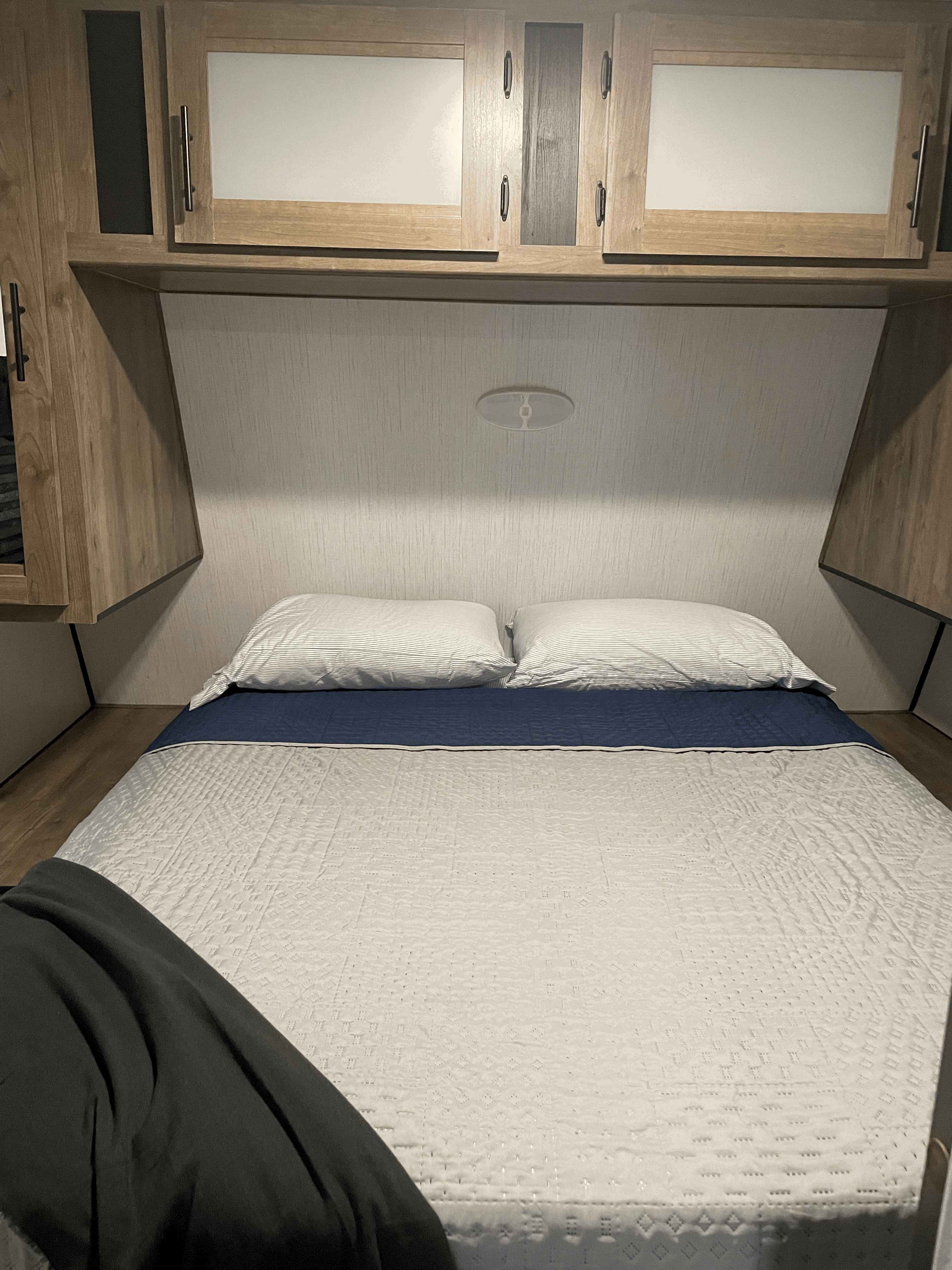 An RV rental bedroom showcasing a comfy bed with striped pillows, blue and white bedding, and wood overhead cabinets.. Heartland RVs Pioneer 2021