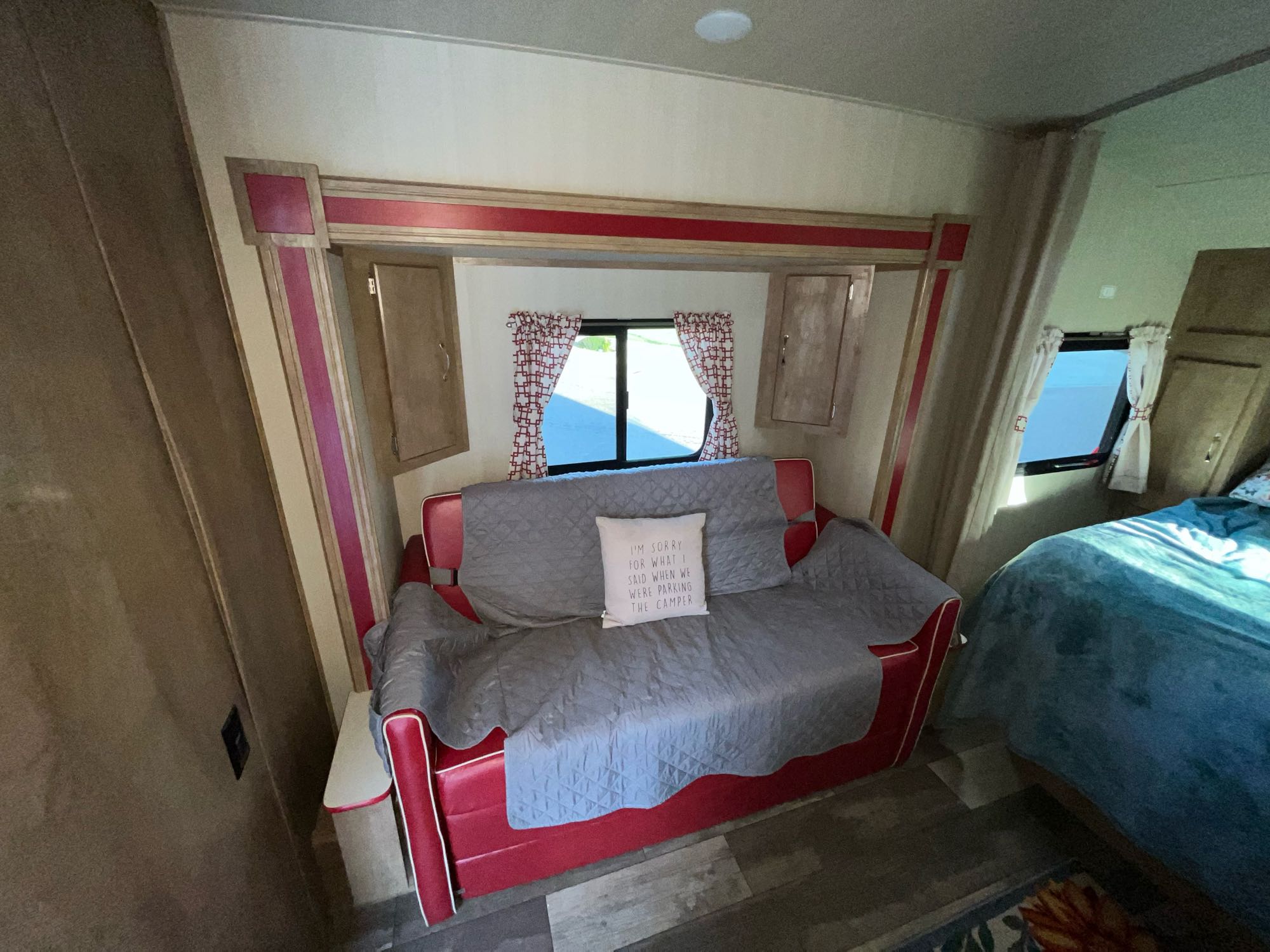 Cozy RV rental interior with a red sofa, humorous pillow, and comfortable bed. Perfect for your next adventure.. Gulf Stream Cruiser 2021