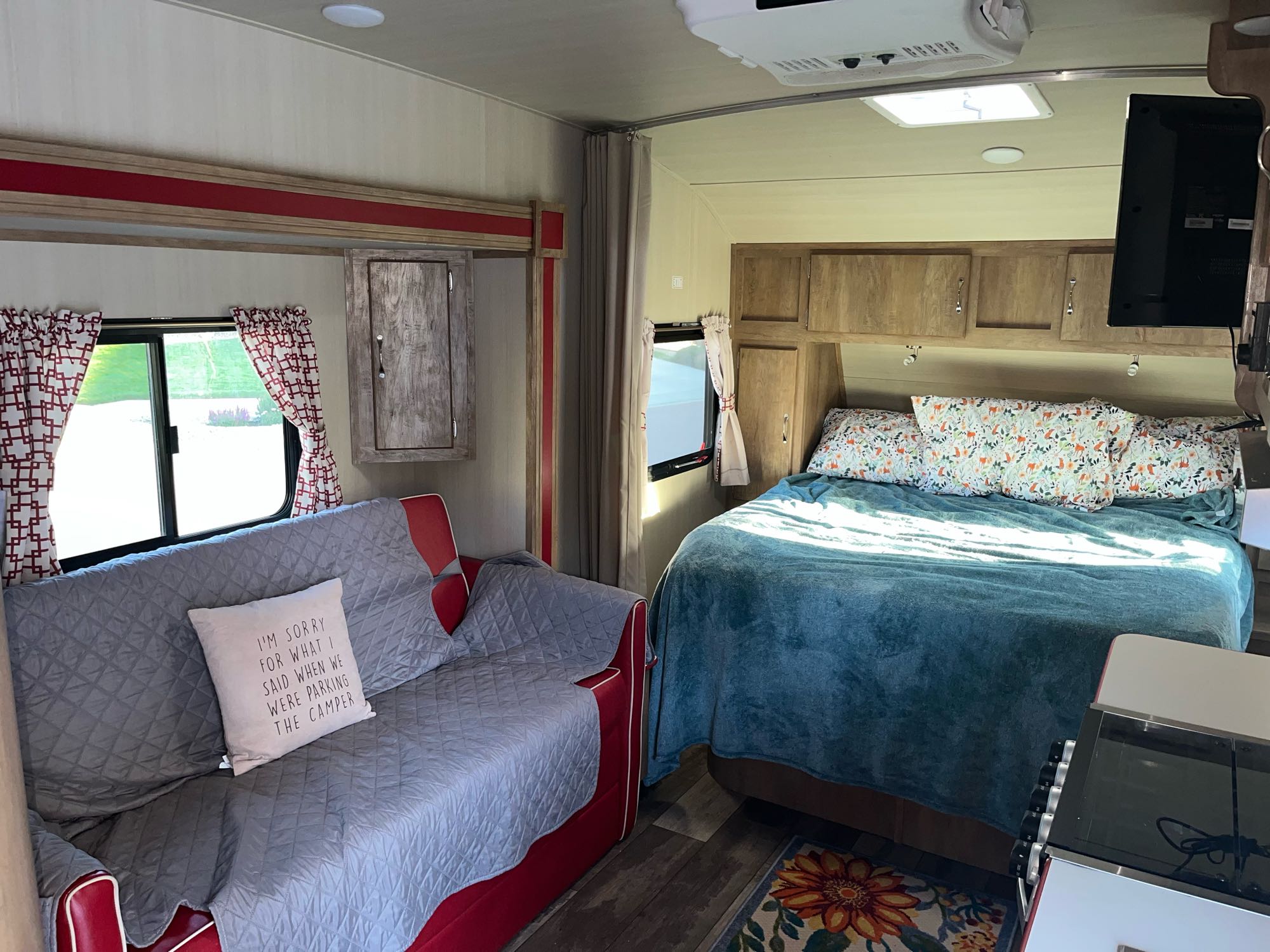 Cozy rv rental interior: red sofa with humorous pillow, bed with patterned bedding, and storage.. Gulf Stream Cruiser 2021
