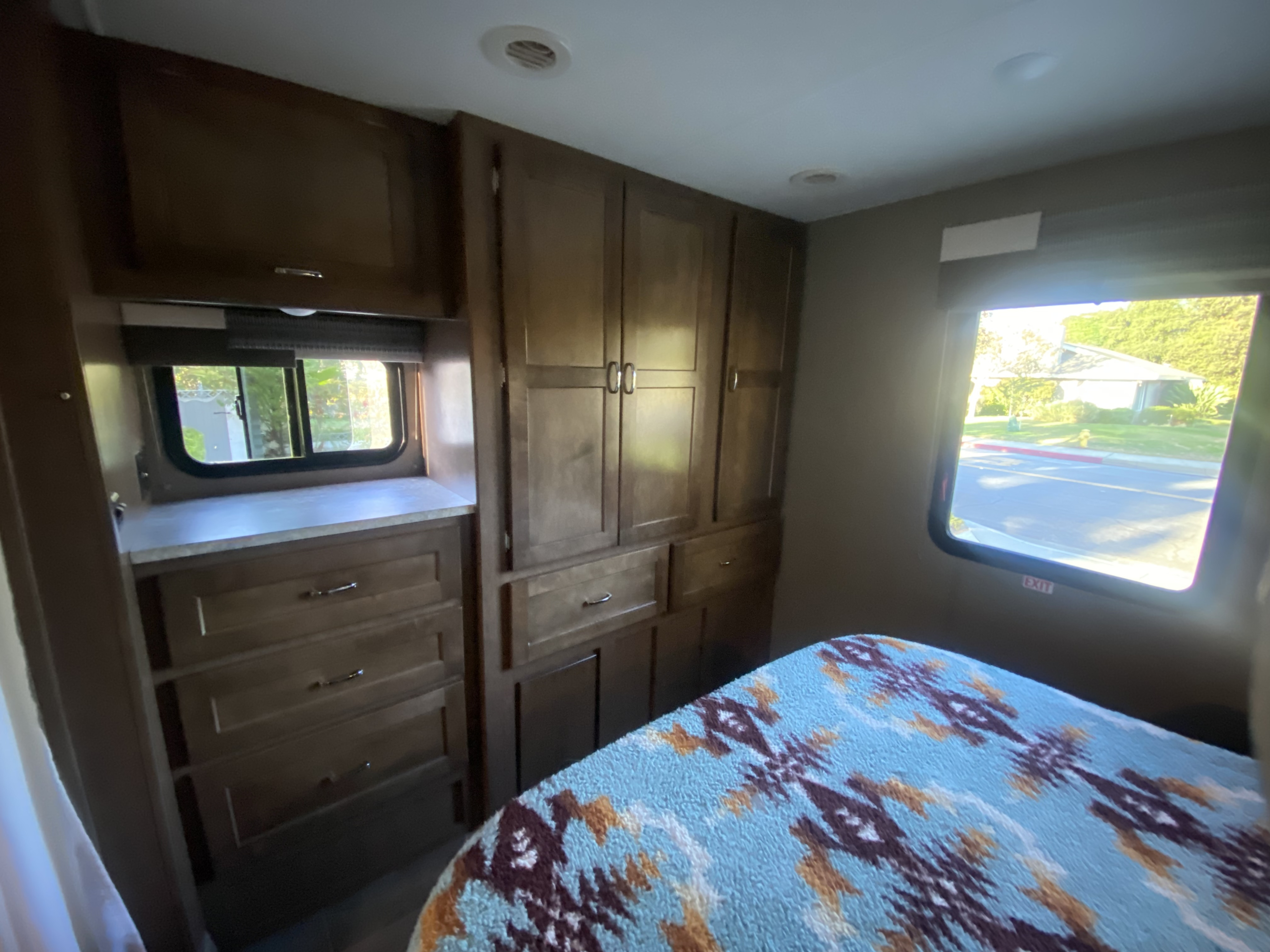 Cozy RV rental bedroom with ample storage and bright windows, featuring a patterned blanket and wood cabinetry.. Winnebago Outlook 2019