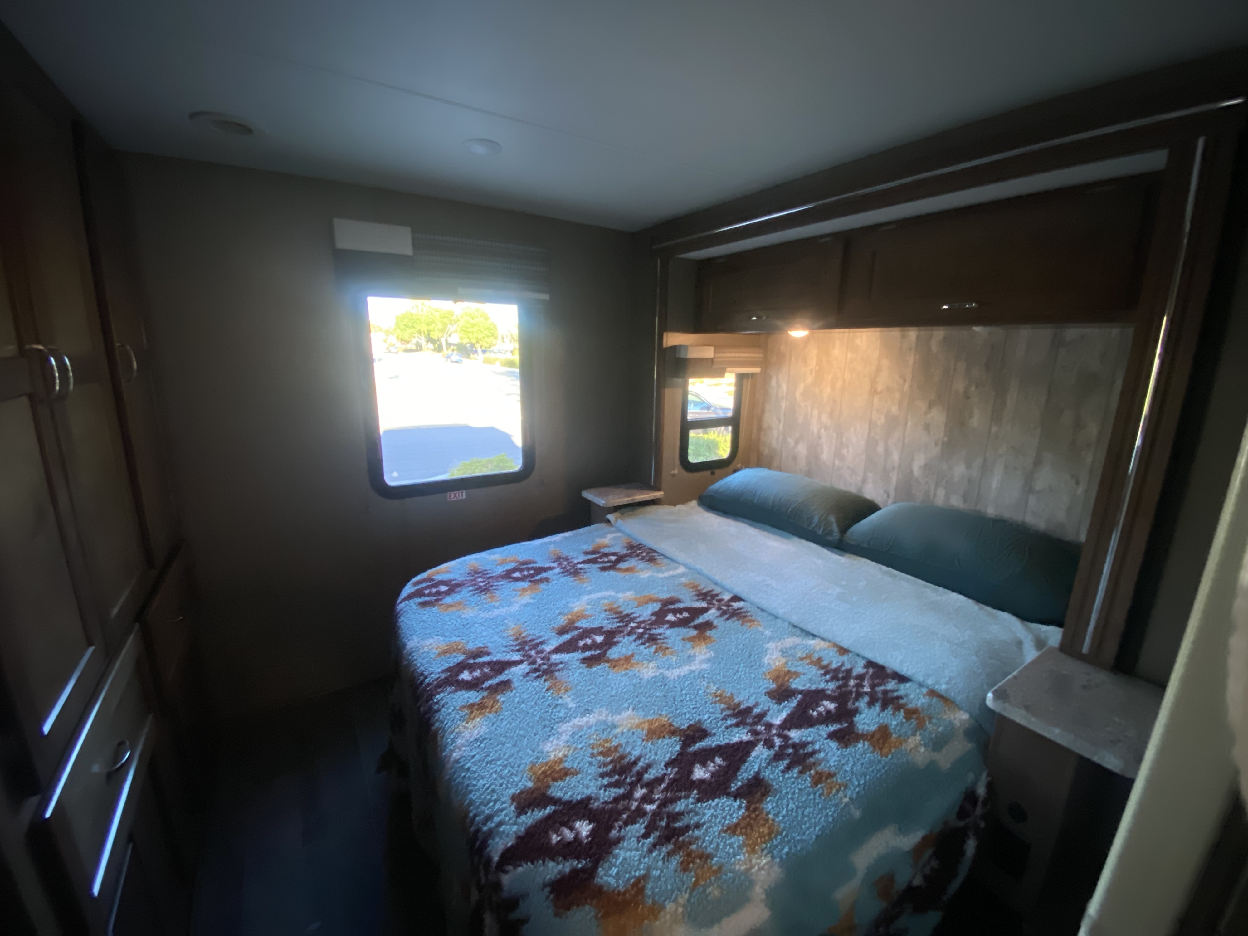 Cozy RV rental bedroom with a patterned bed, pillows, and bright windows, perfect for travel.. Winnebago Outlook 2019