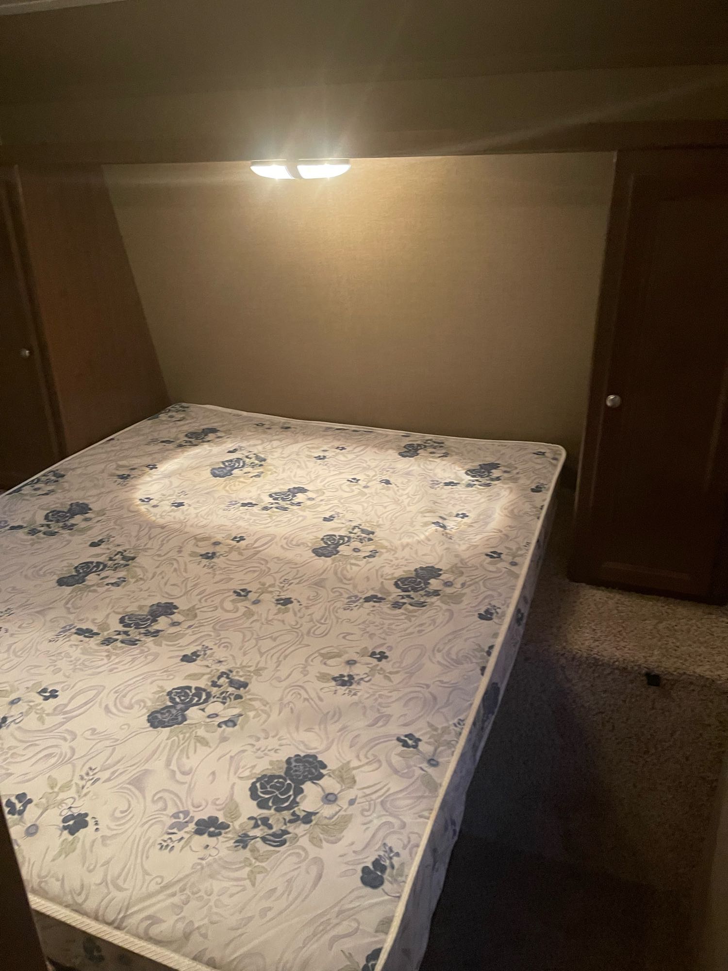 Compact RV rental bedroom with floral mattress, built-in storage, and overhead light for a comfortable stay.. Keystone Hideout 2016