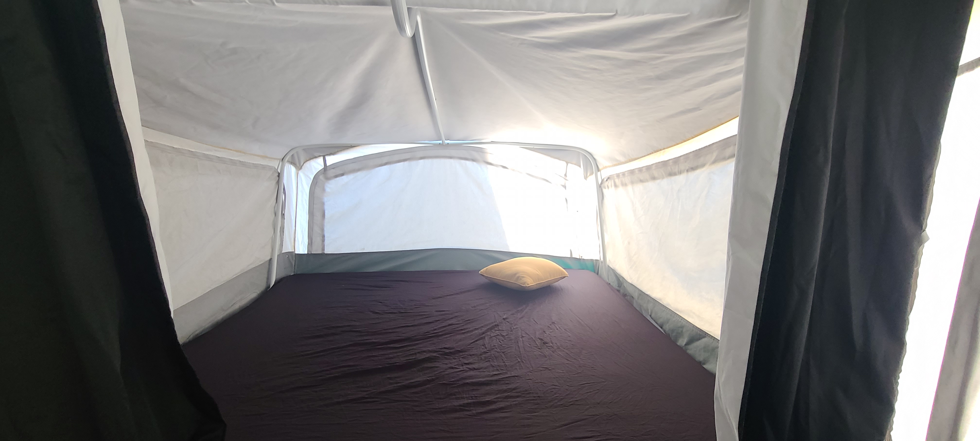 Inside an RV rental: a pop-up camper's sleeping area with dark mattress, yellow pillow, and white fabric walls/ceiling.. Coleman Grand Tour 2001