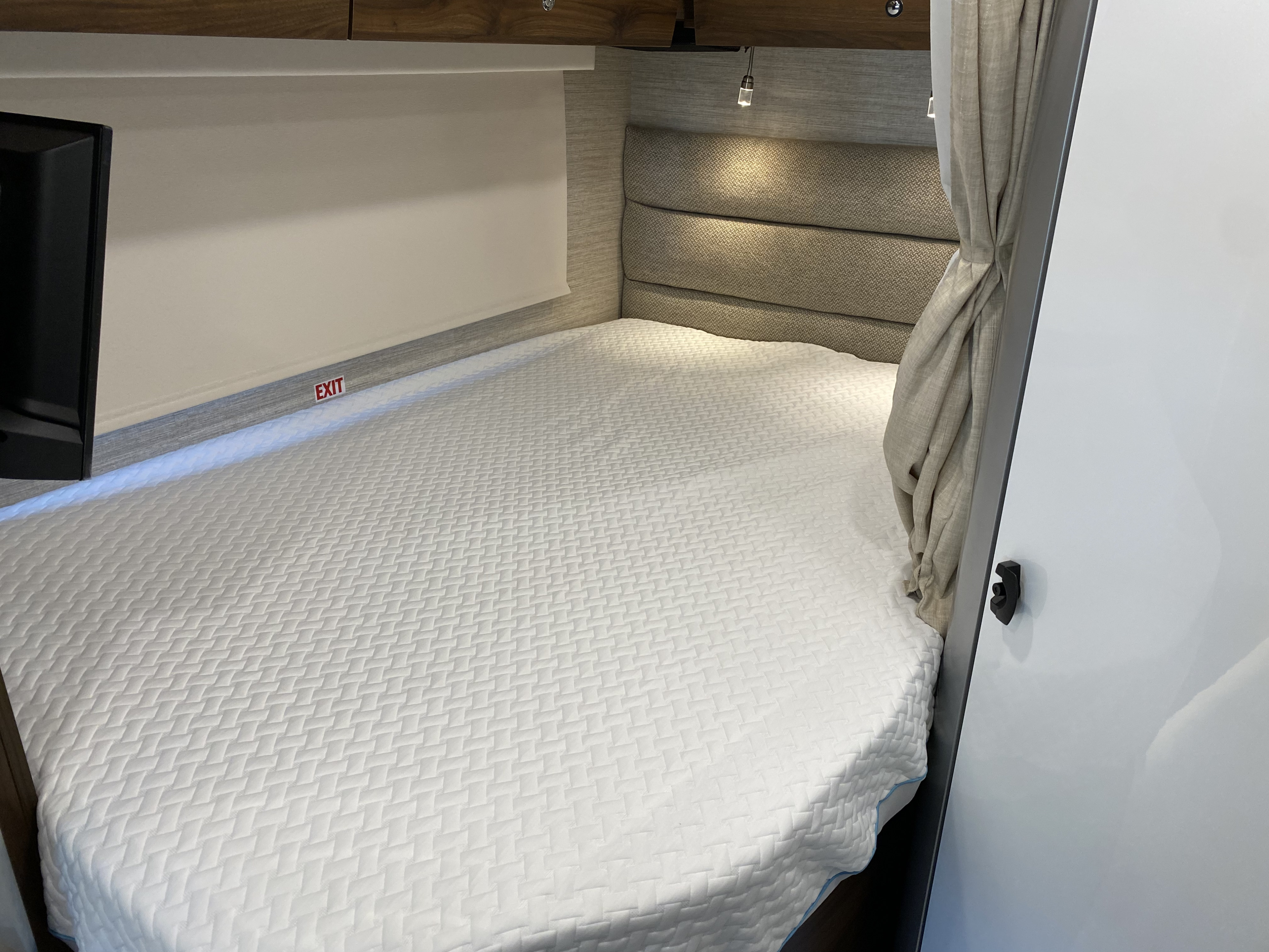 Comfortable rv rental sleeping area with a fresh white bed, cushioned headboard, and emergency exit.. Winnebago View 2022