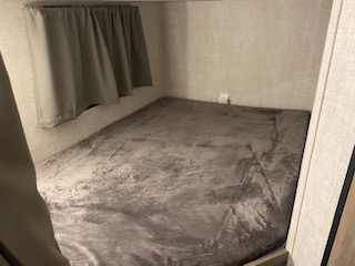 Inside an RV rental: a compact bedroom with a gray bed, window, and curtain, designed for comfortable travel.. Gulf Stream Enlighten 2022