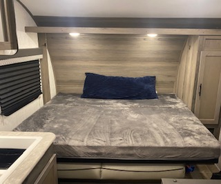Inside this **rv rental** is a cozy bedroom with a bed, grey blanket, blue pillow, and overhead lights, perfect for travel comfort.. Gulf Stream Enlighten 2022