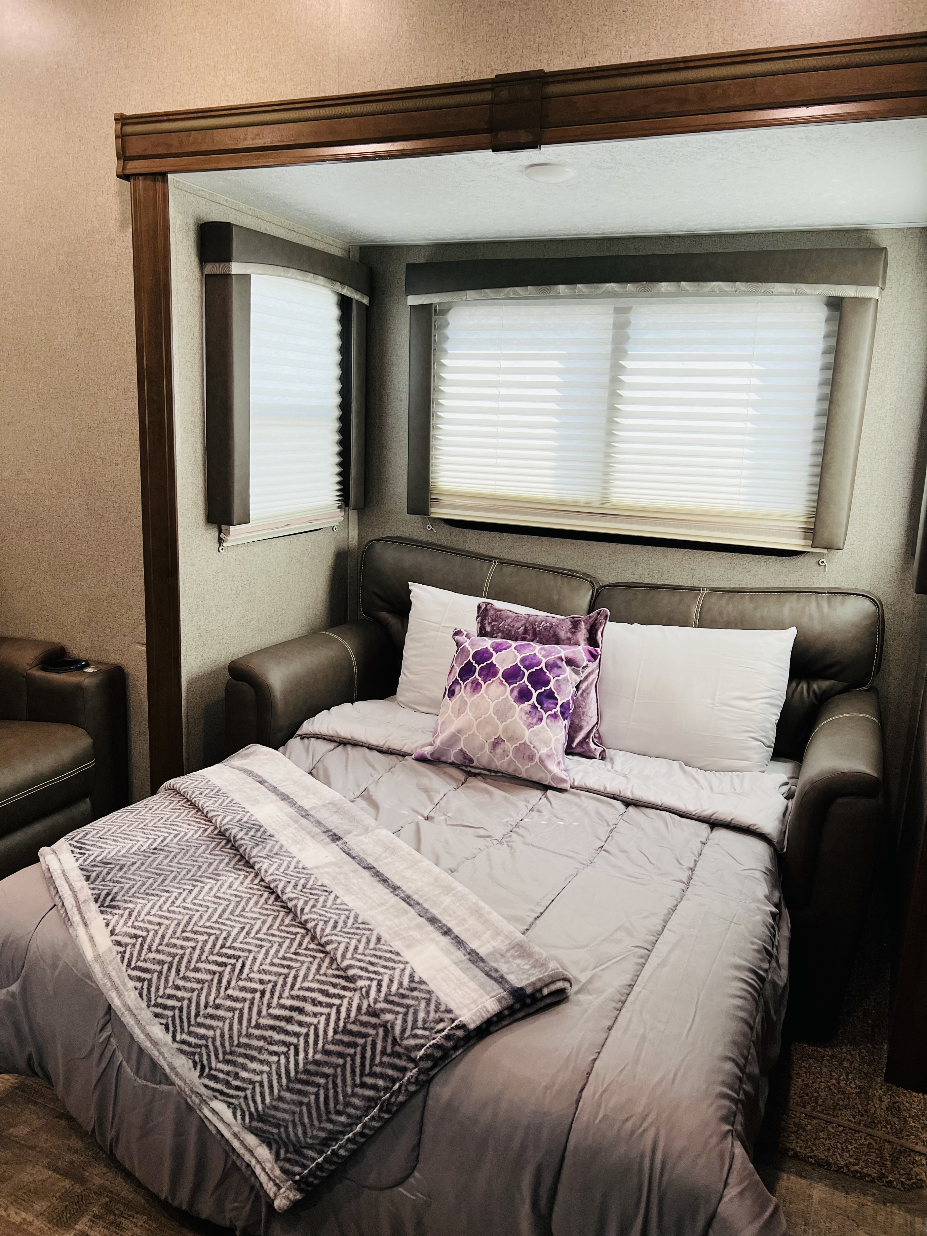 Experience comfort in our RV rental: a plush sofa bed with purple pillows and cozy blankets, perfect for your journey.. Forest River Rockwood Ultra Lite 2020