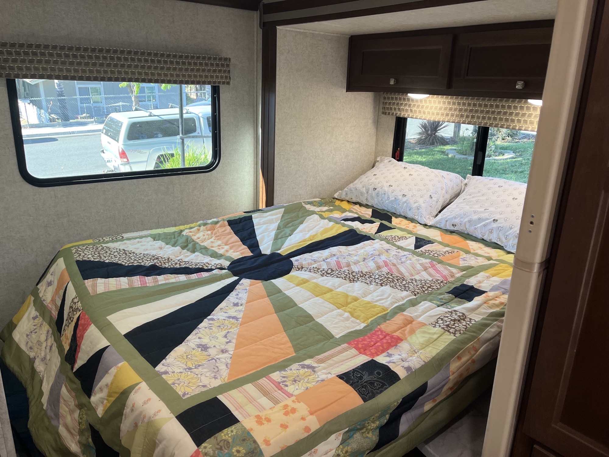 Cozy RV rental bedroom with a colorful quilt on the bed, two pillows, and windows showing the outdoors.. Forest River Sunseeker LE 2019