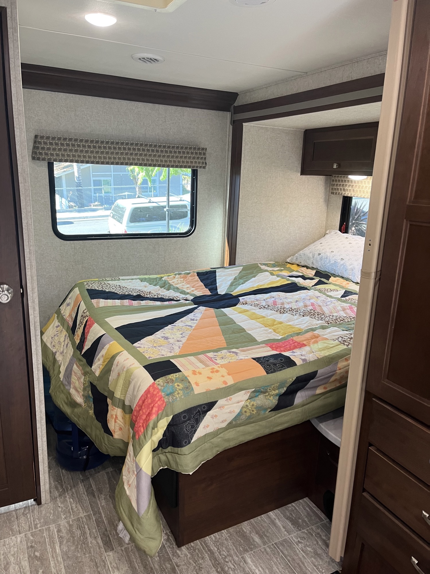 Cozy RV rental bedroom with a colorful quilt, a large window view, and integrated storage.. Forest River Sunseeker LE 2019